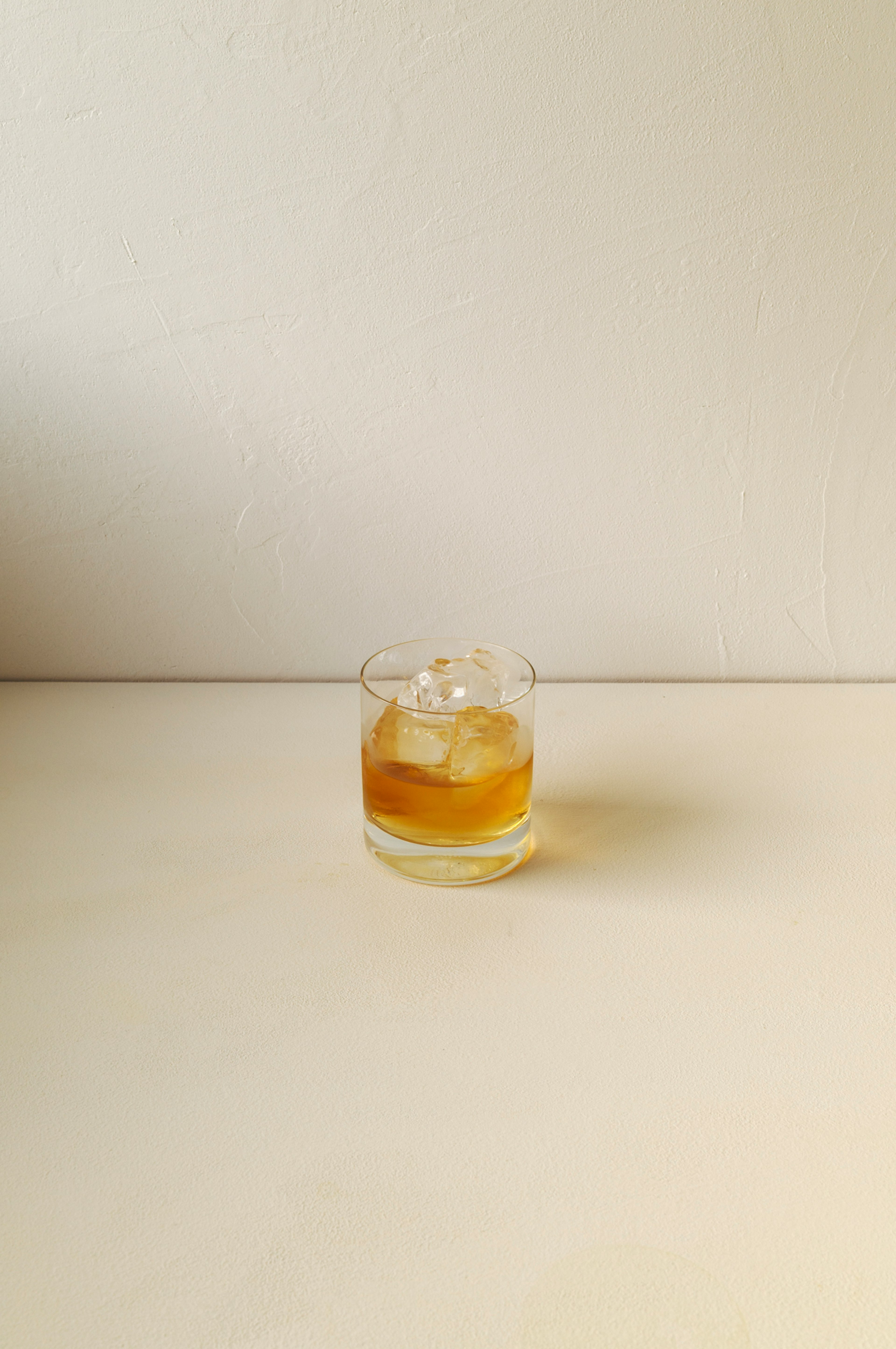 Una imagen simple de un vaso transparente con whisky y hielo