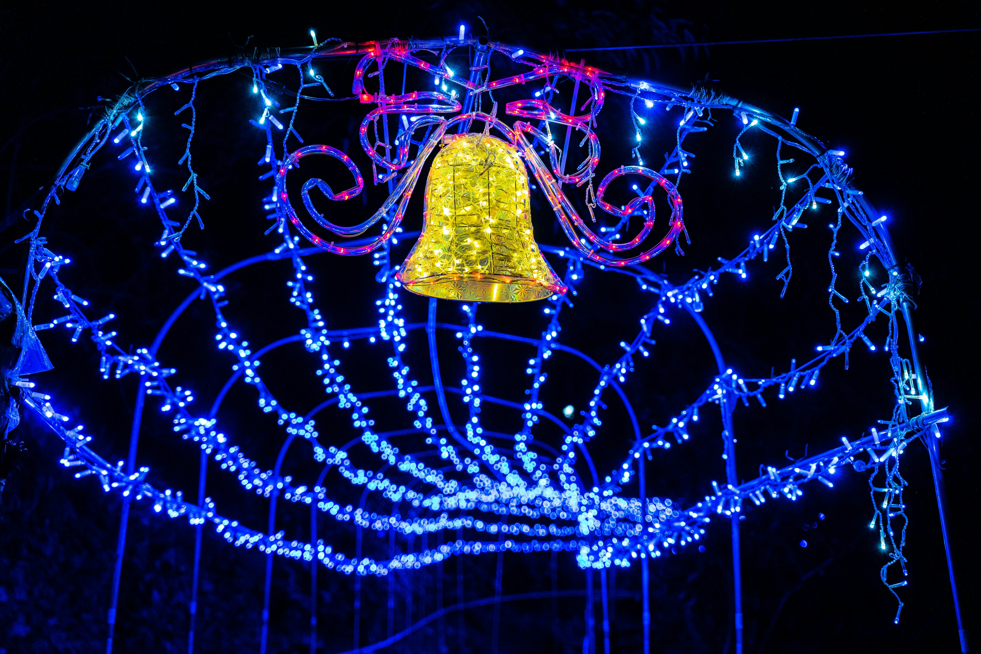 A decorative bell in gold surrounded by blue and purple lights