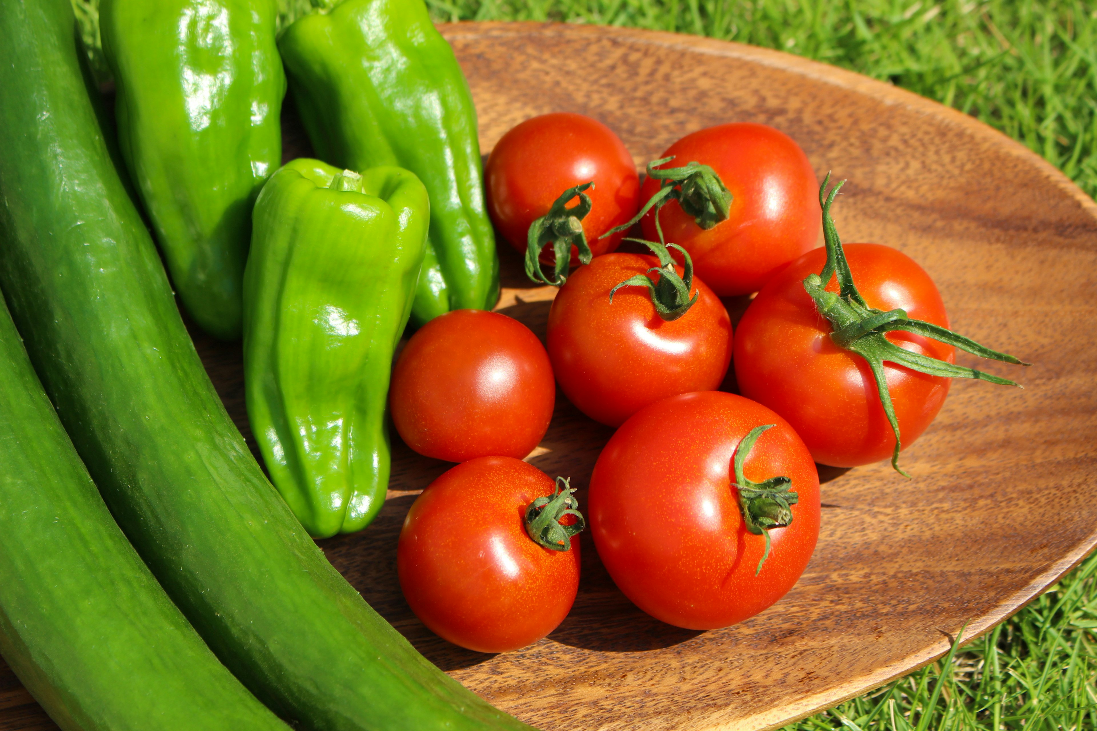 Fresh tomatoes, green peppers, and cucumbers arranged on a wooden platter