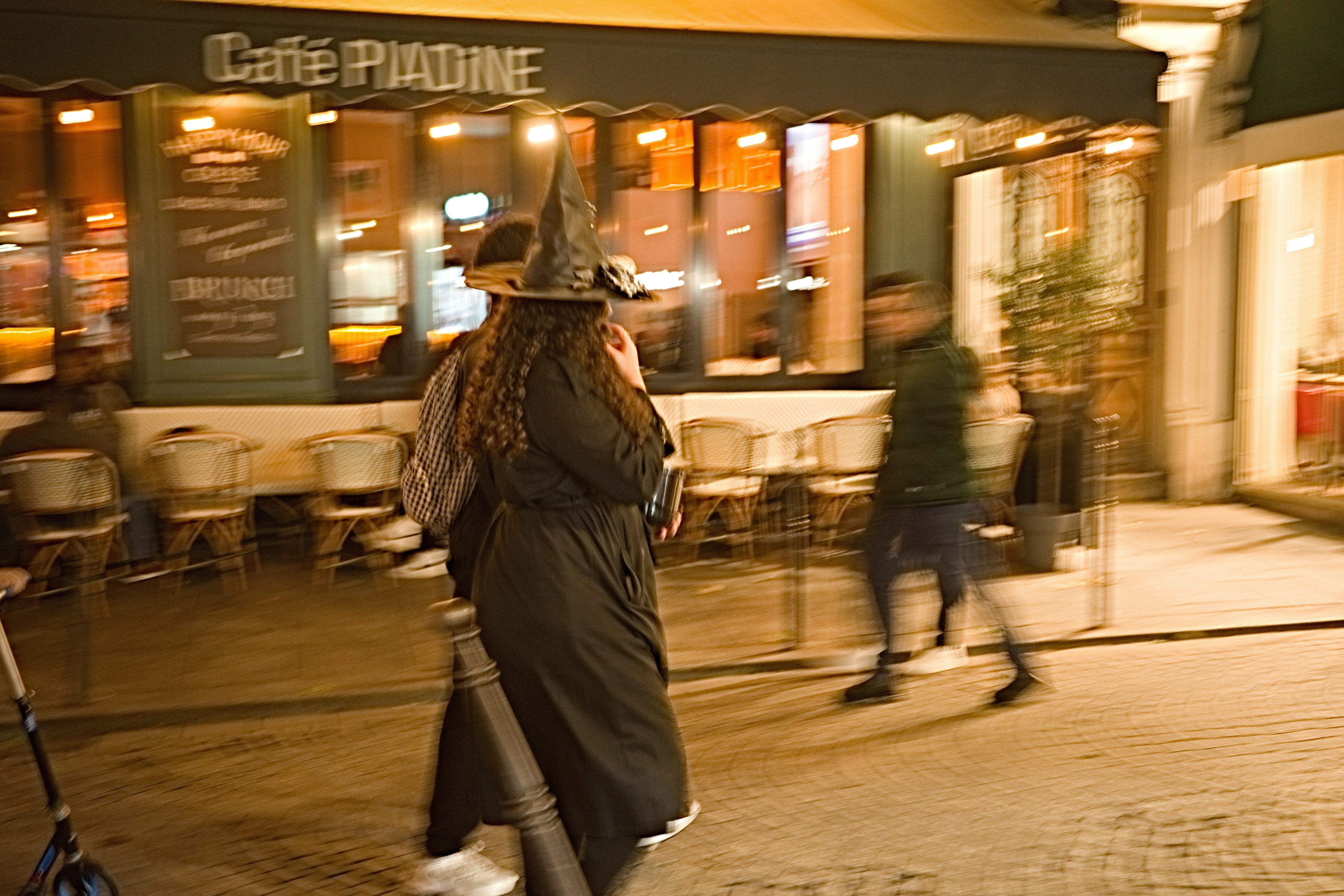 A woman in a witch costume walking past a café at night