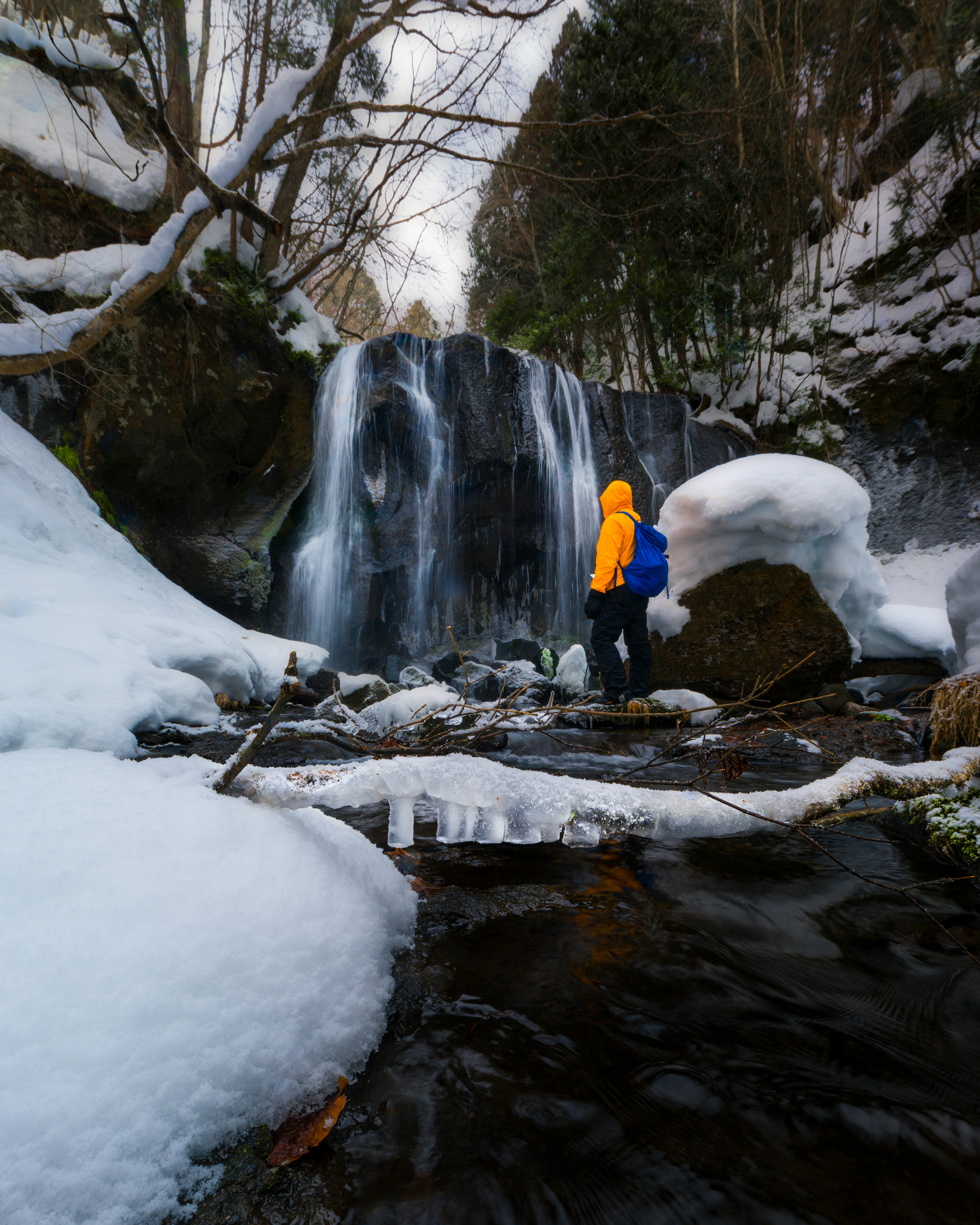 Person in orange jacket standing in front of snow-covered waterfall