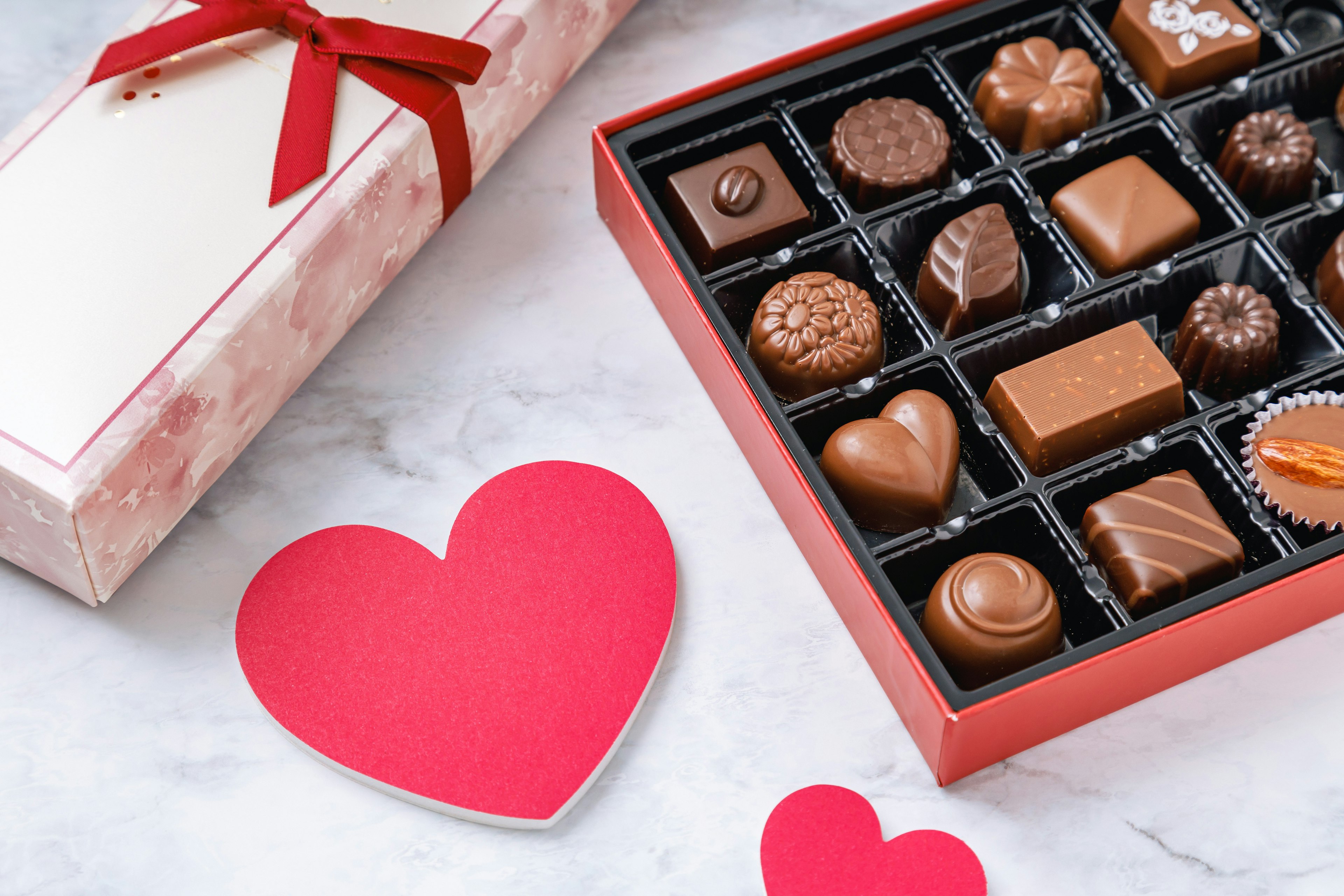 Una caja de chocolates surtidos con una tarjeta en forma de corazón rojo cerca