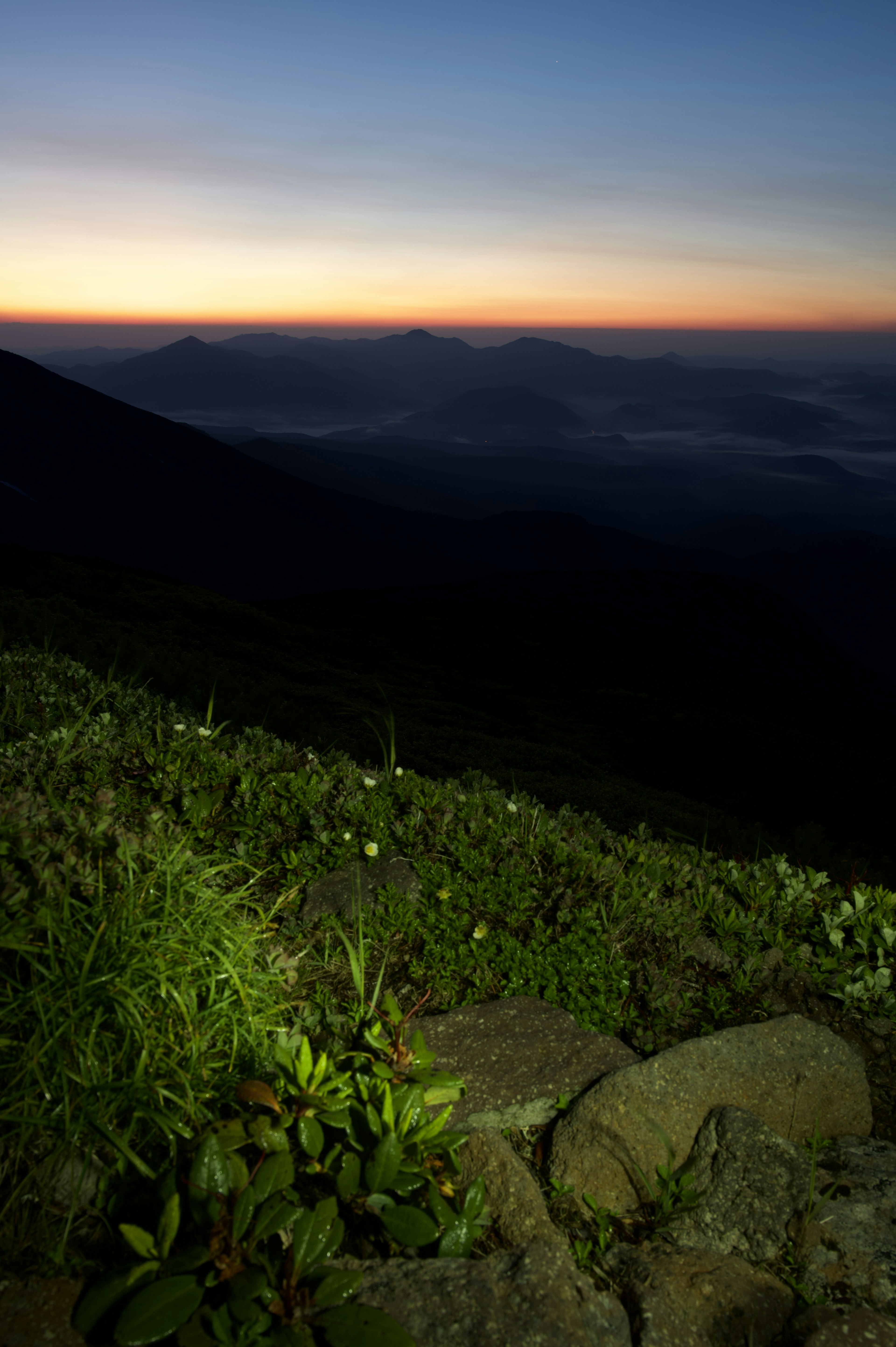 Pemandangan gunung saat matahari terbenam dengan rumput dan batu di latar depan