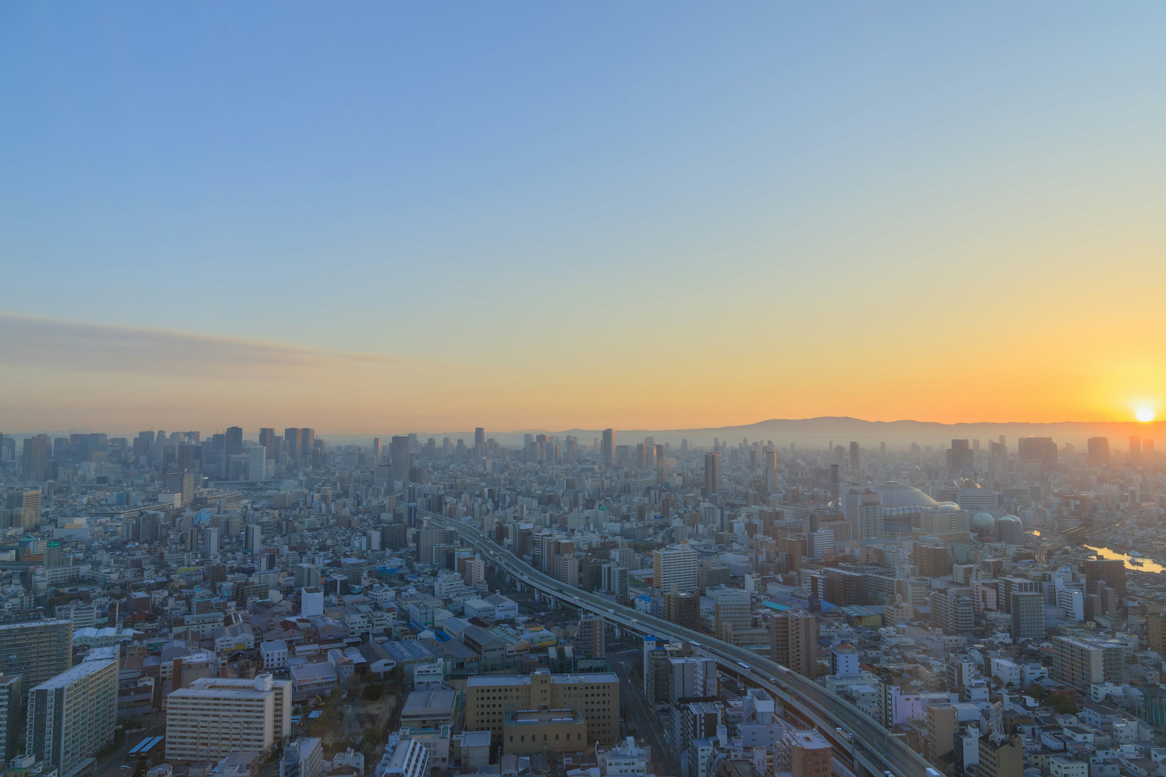 Panoramic view of Osaka at sunset featuring skyscrapers and roads