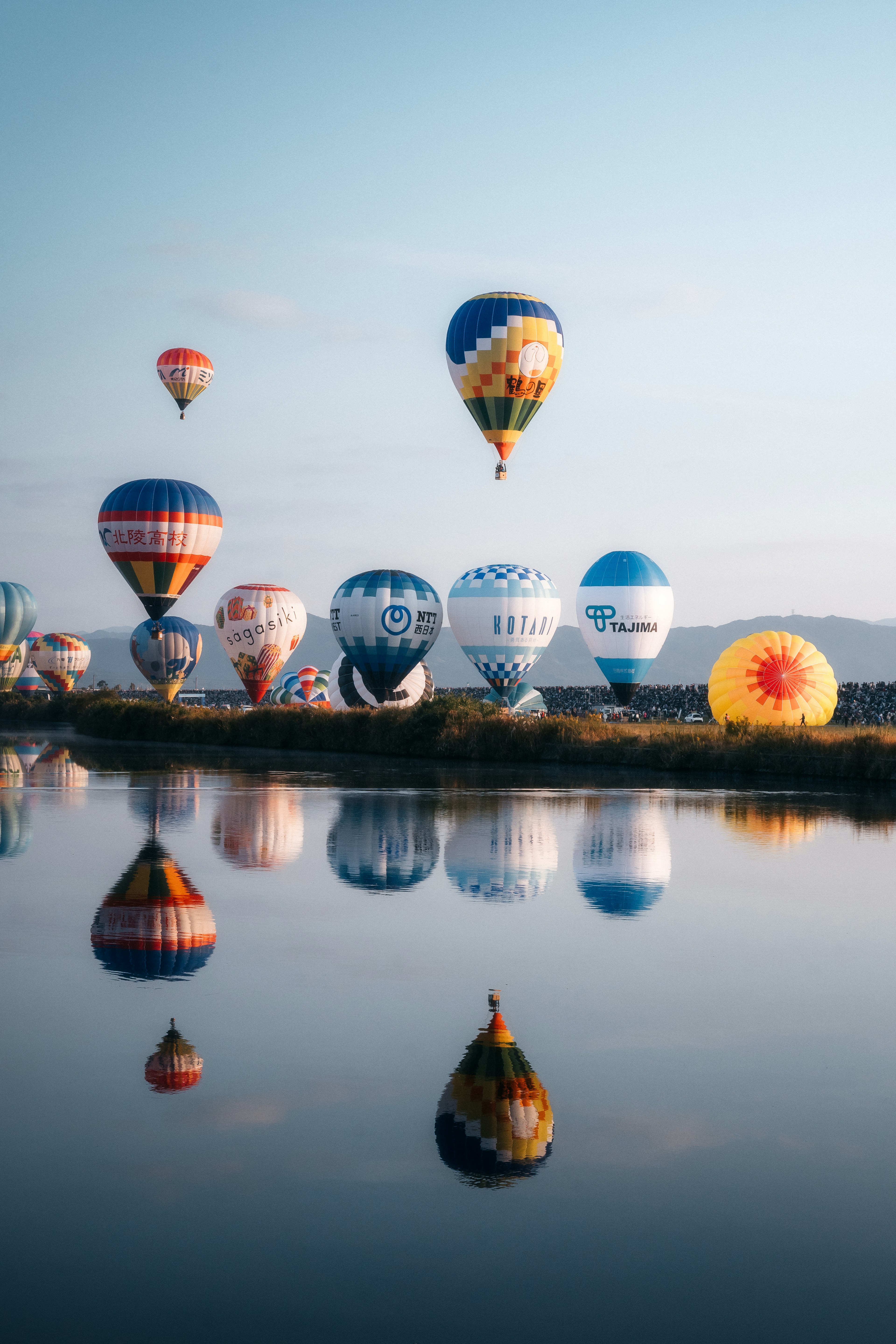 Palloni aerostatici colorati che fluttuano nel cielo blu con riflessi nell'acqua