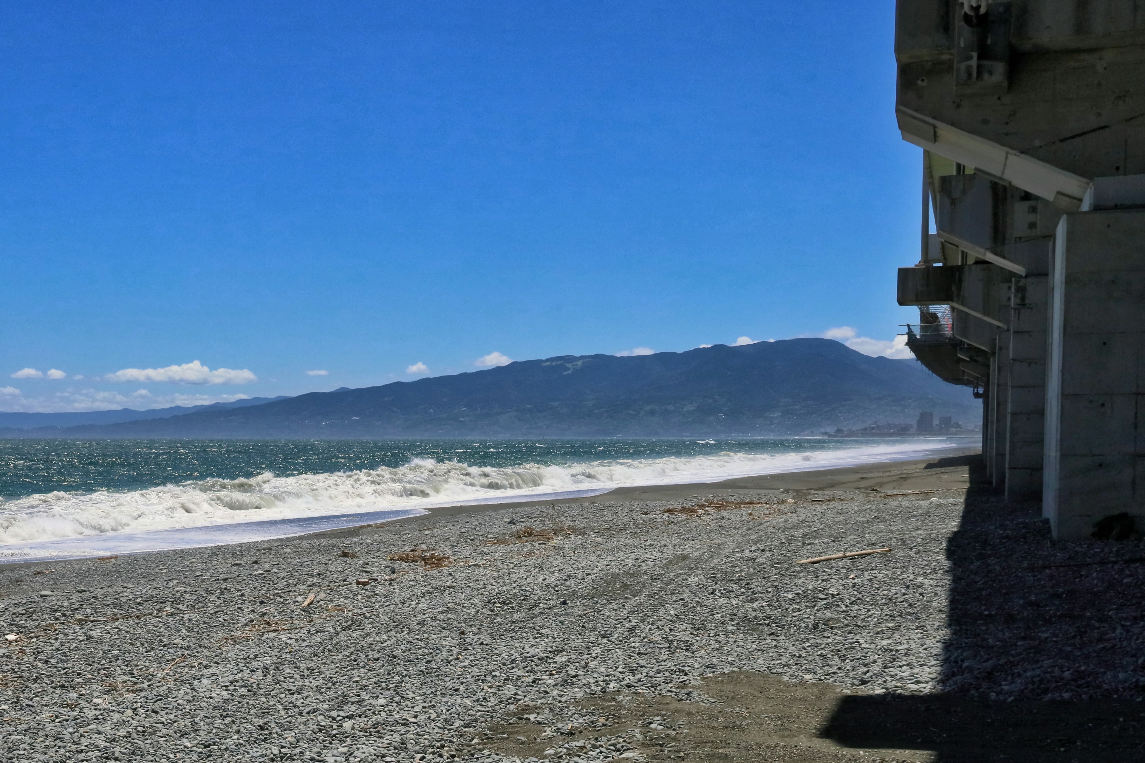 Scène de plage avec ciel bleu et vagues, bâtiment le long de la côte