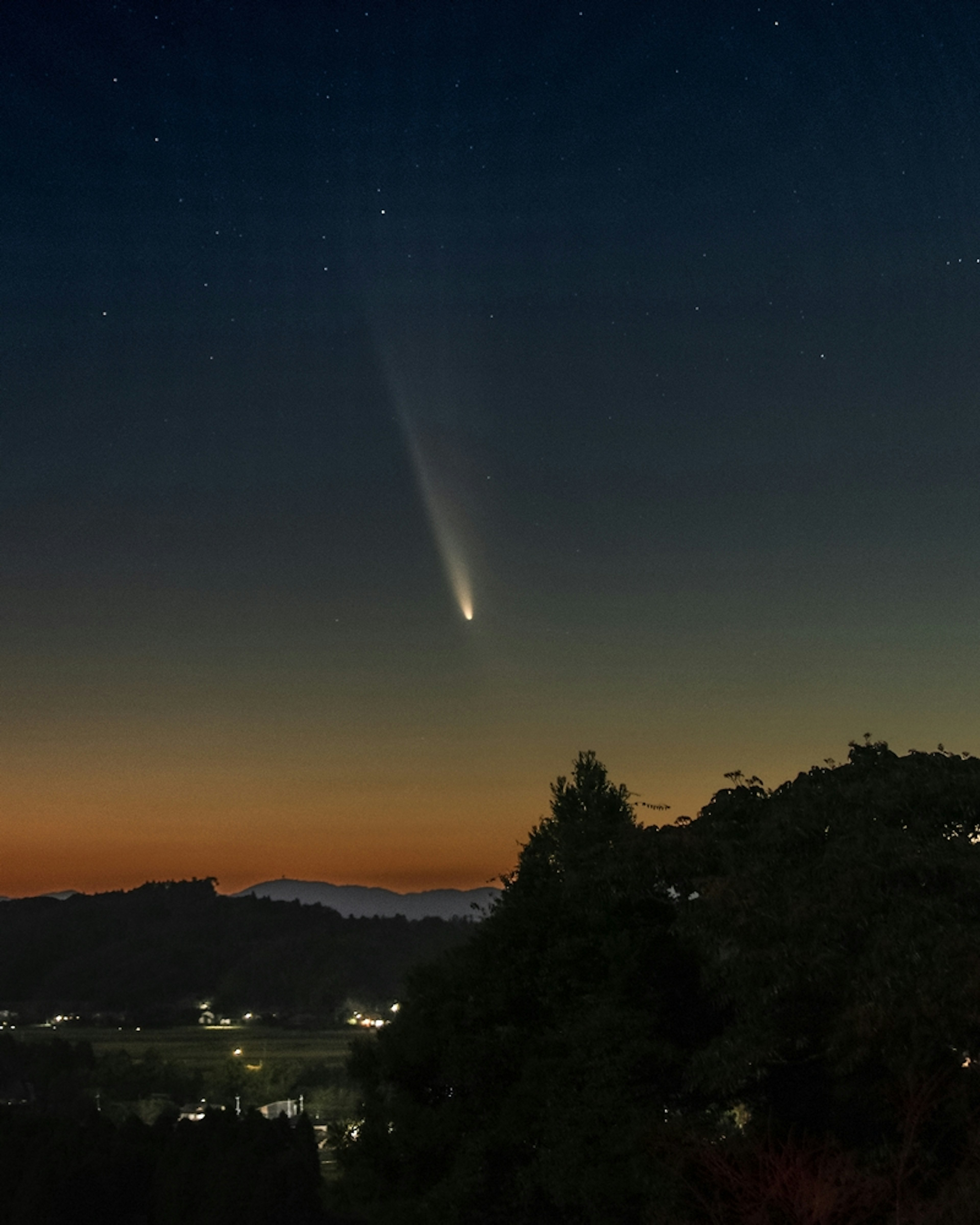 Comet shining in the night sky with a colorful sunset landscape