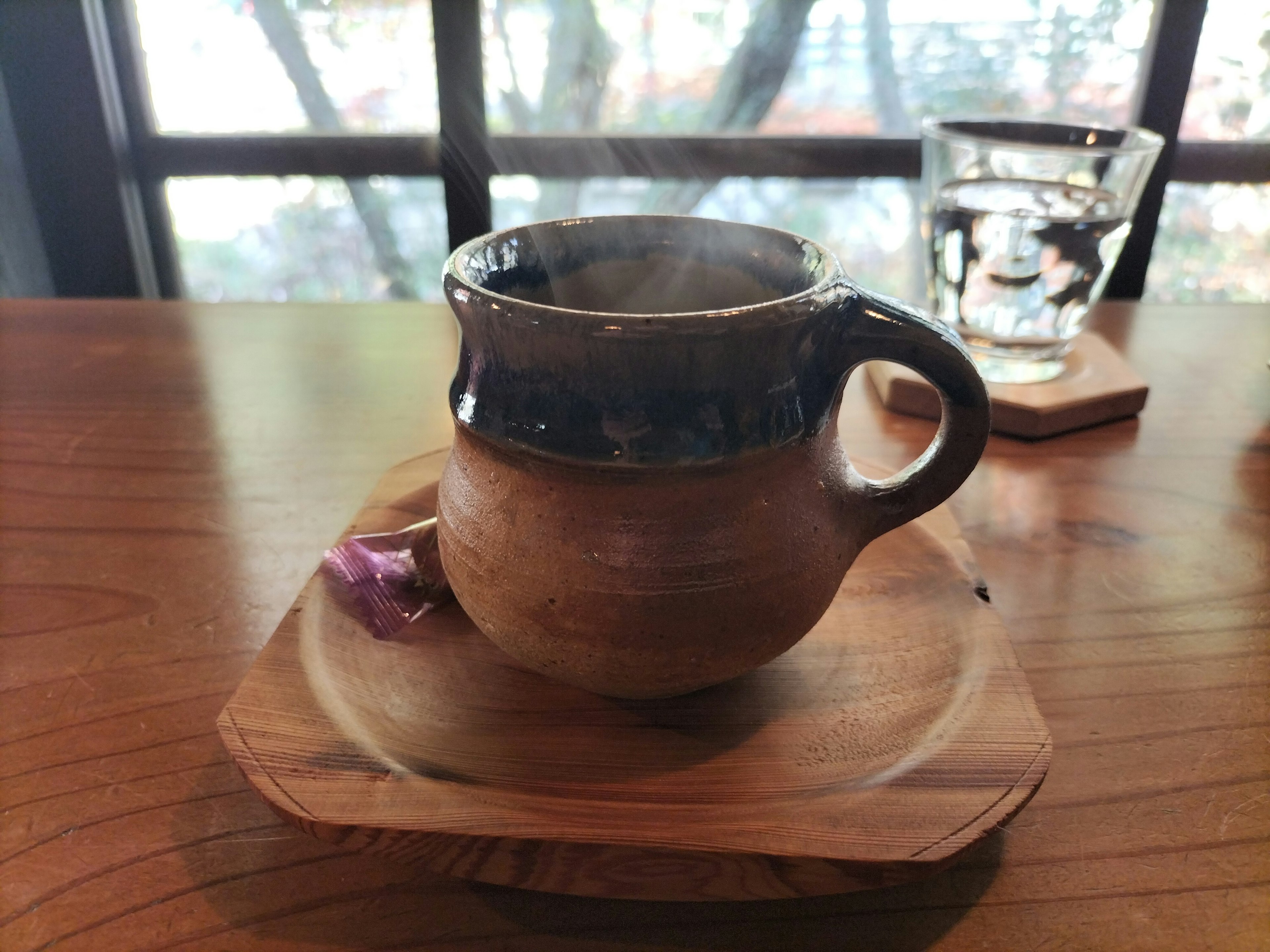 A steaming ceramic cup on a wooden plate with a delicate flower beside it