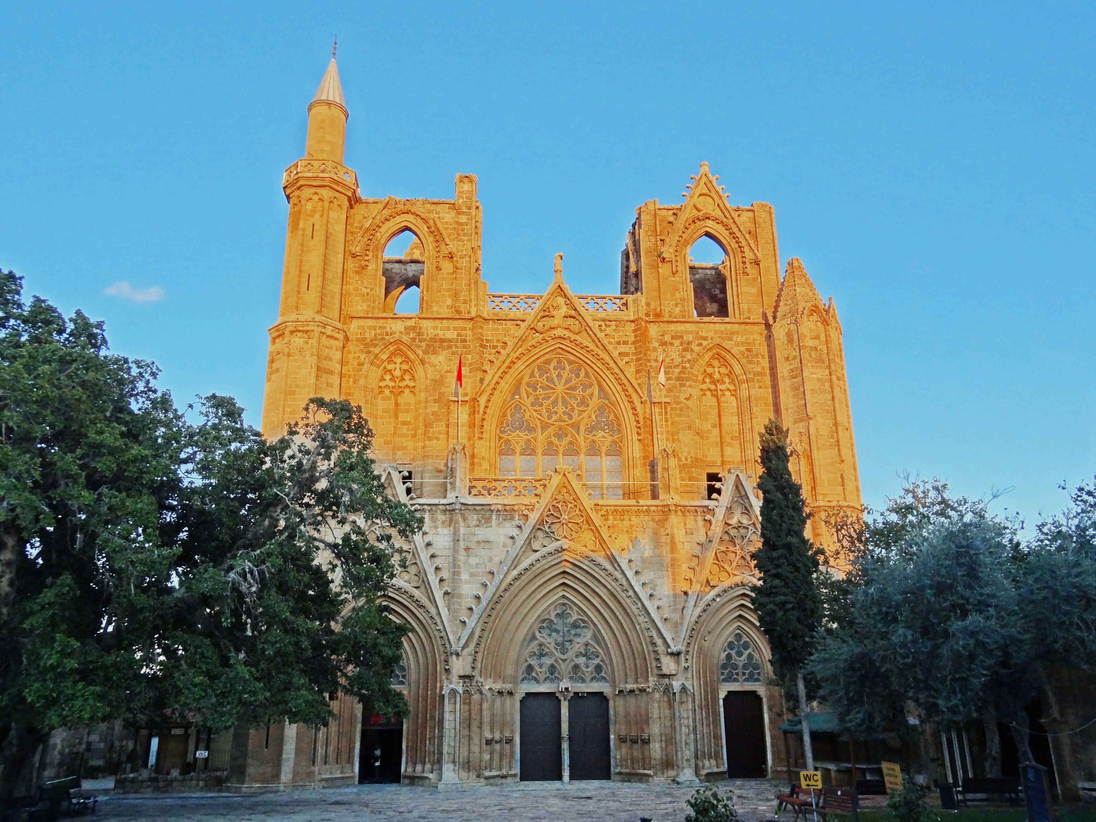 Esterno maestoso di una chiesa in stile gotico sotto un cielo blu brillante circondato da una lussureggiante vegetazione