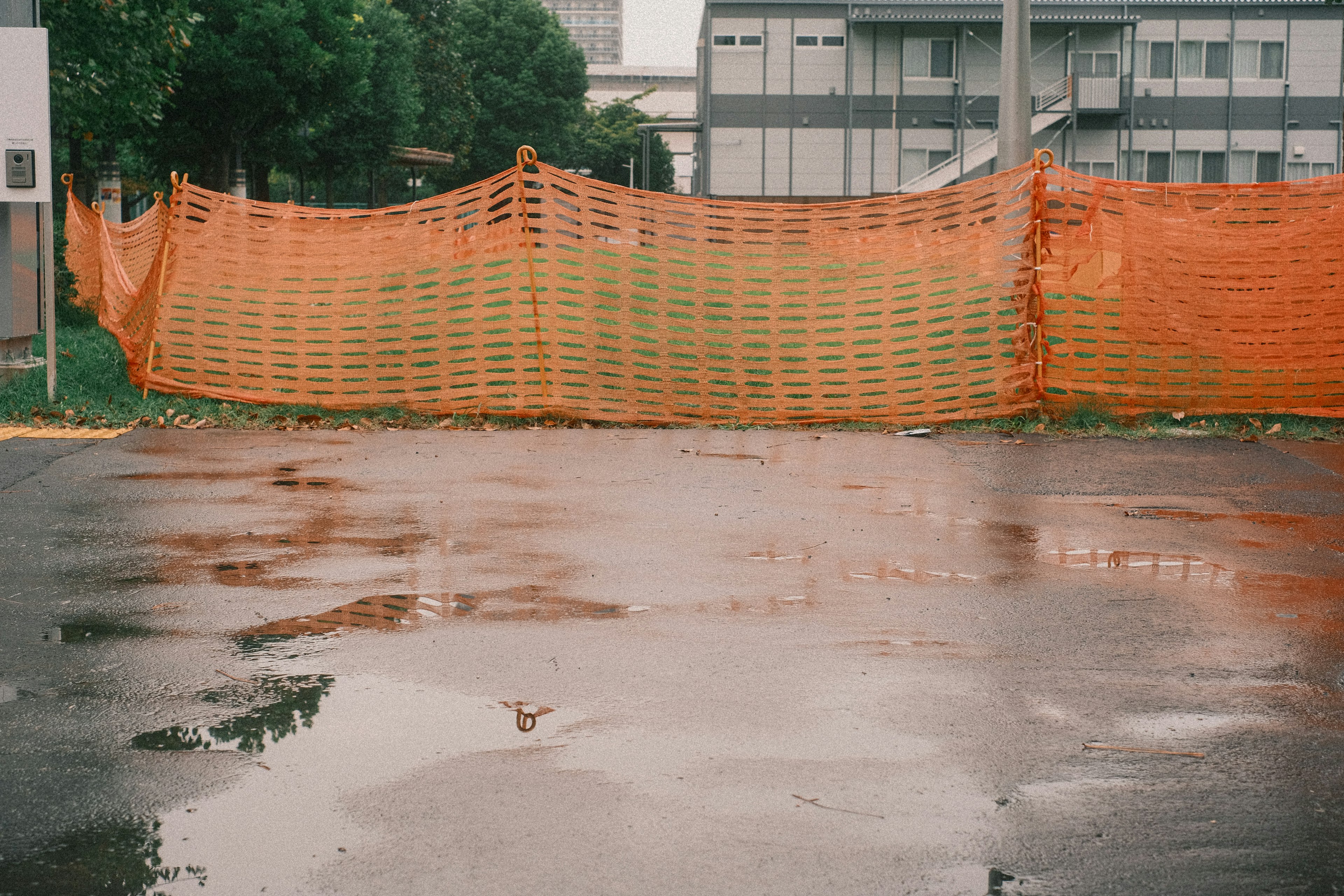 Eine Ansicht von nassem Asphalt mit einem orangefarbenen Zaun im Vordergrund