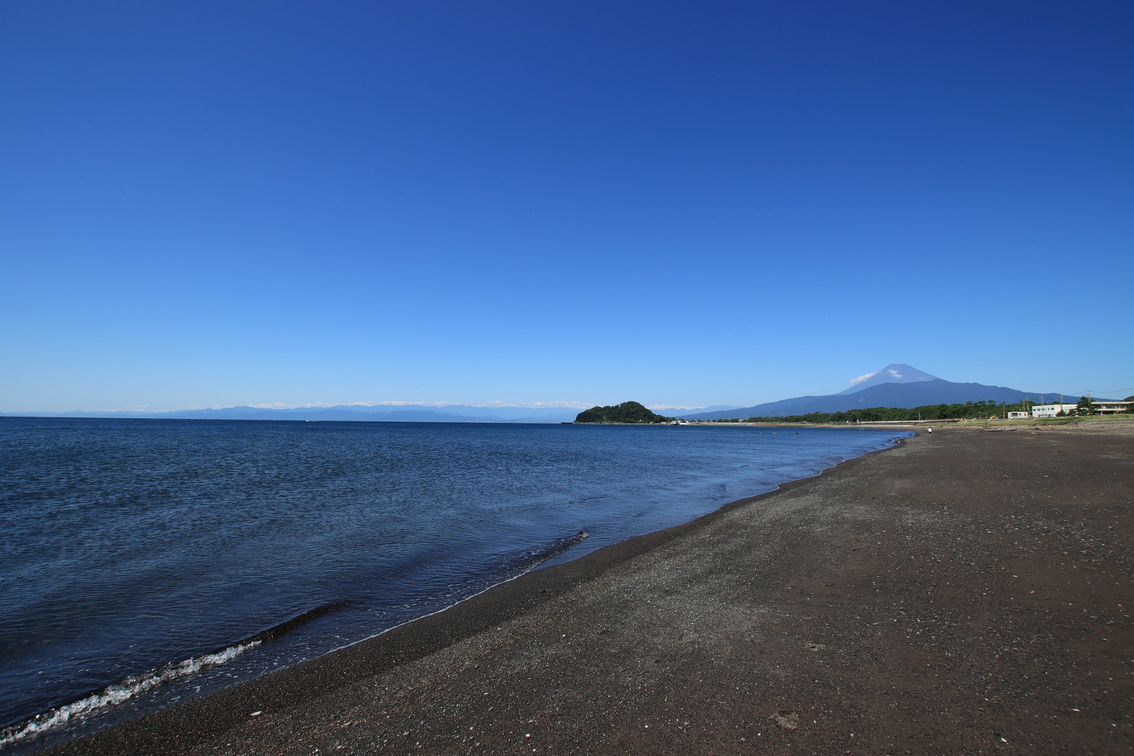 Vue pittoresque du ciel bleu et de la mer plage de sable noir avec une montagne au loin