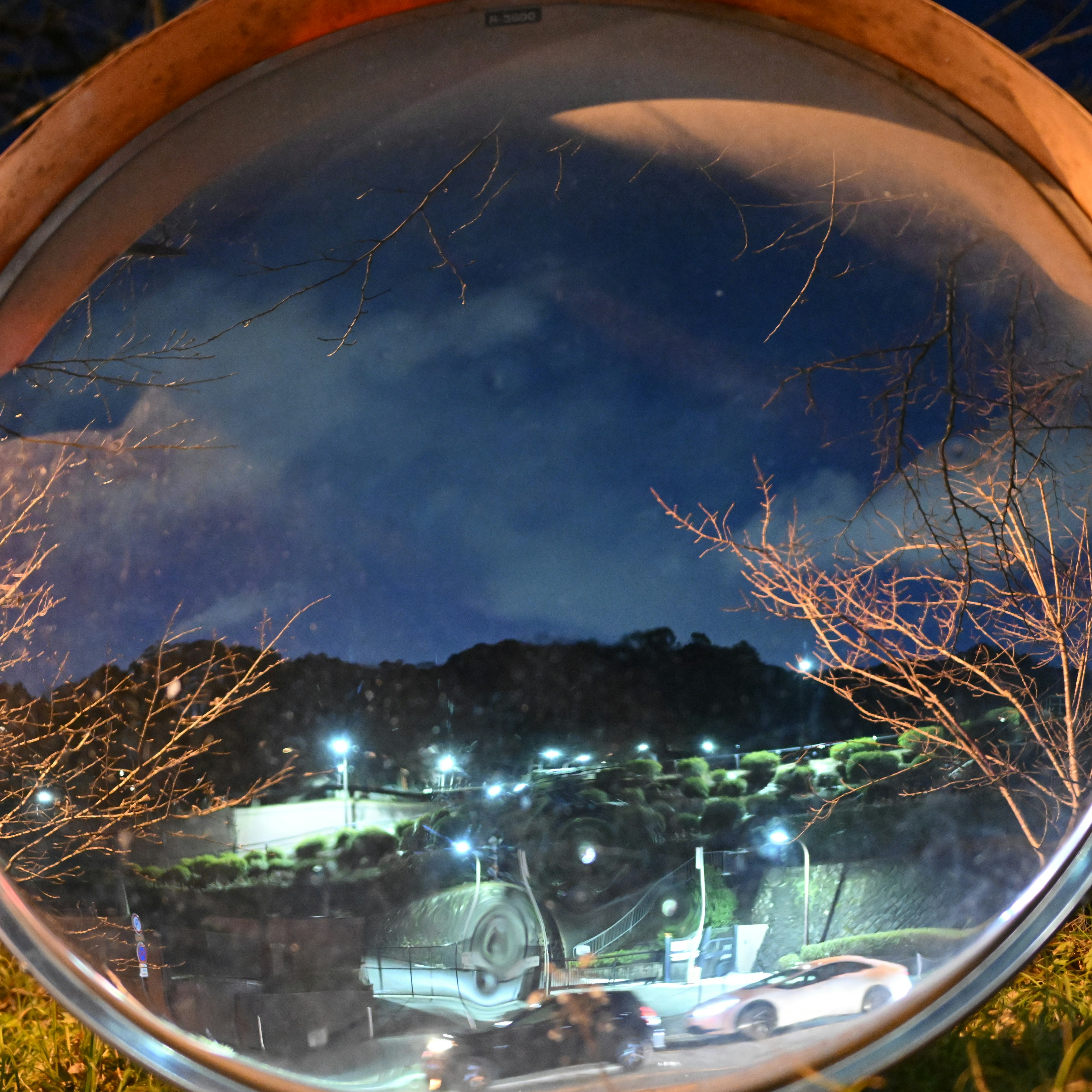 Round mirror reflecting a night sky with bright streetlights and distant hills