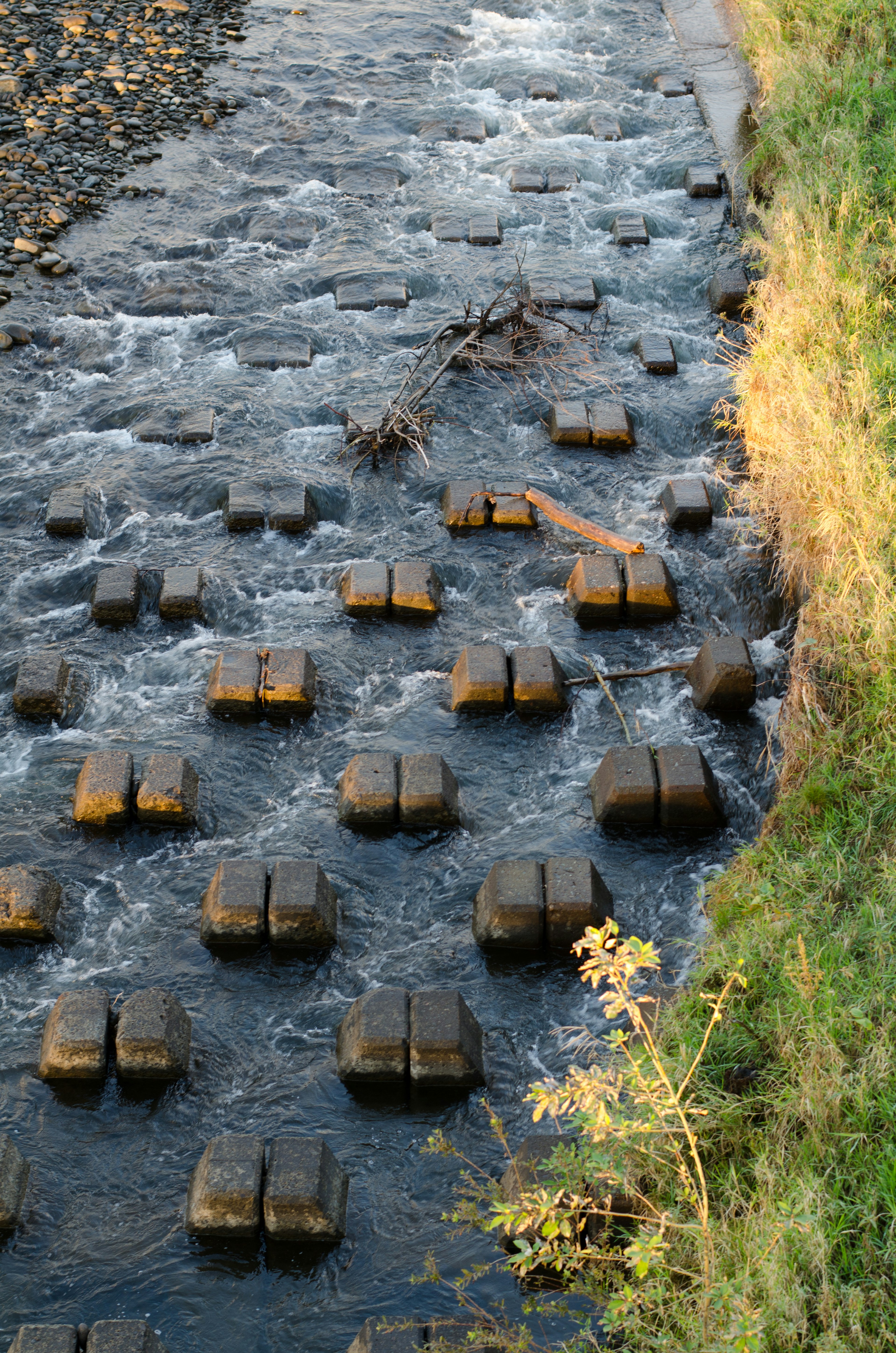 Bloques de concreto dispuestos en un patrón a lo largo del agua corriente con hierba cerca