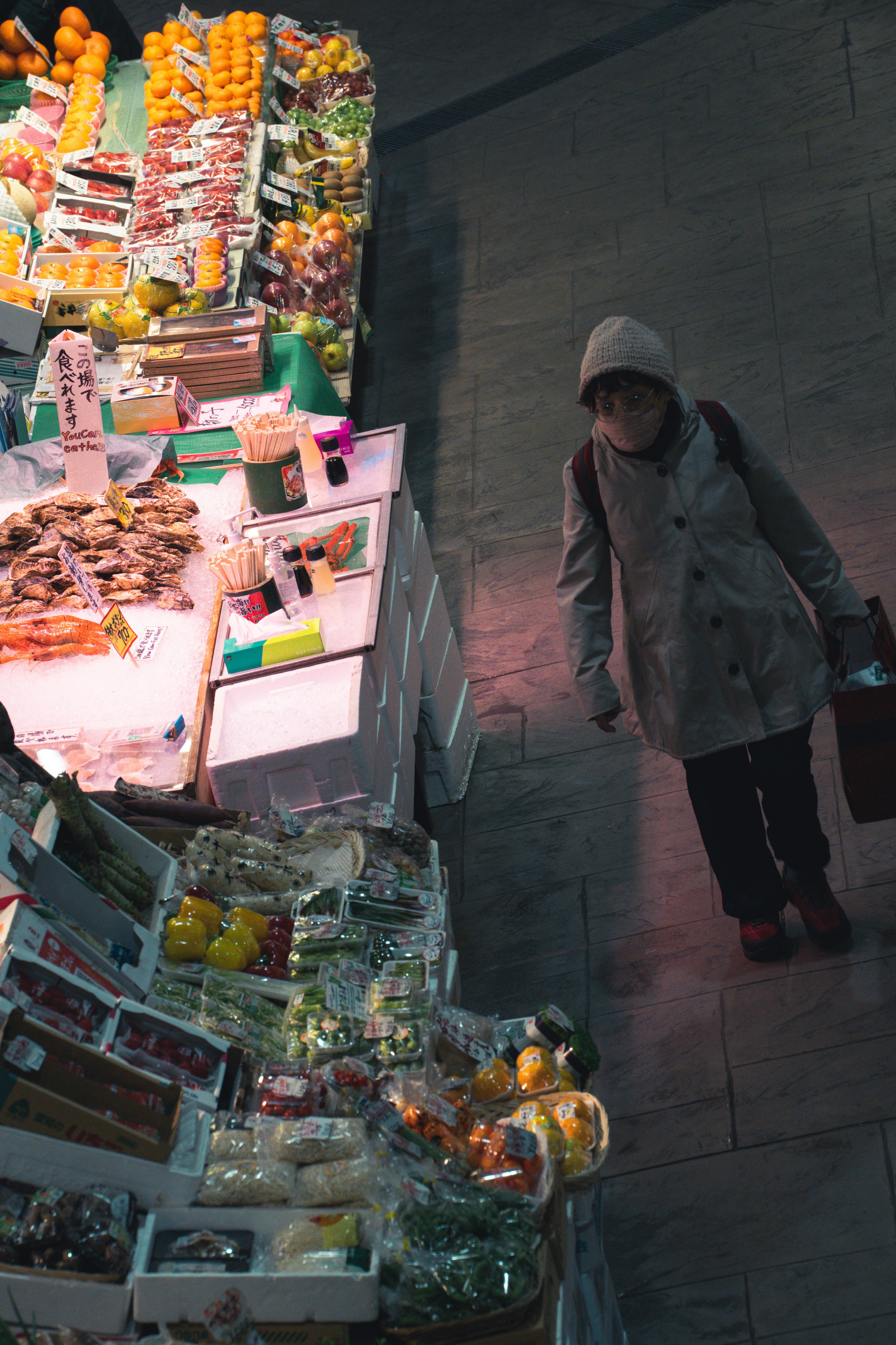 Una mujer observando productos en un mercado con frutas y verduras coloridas