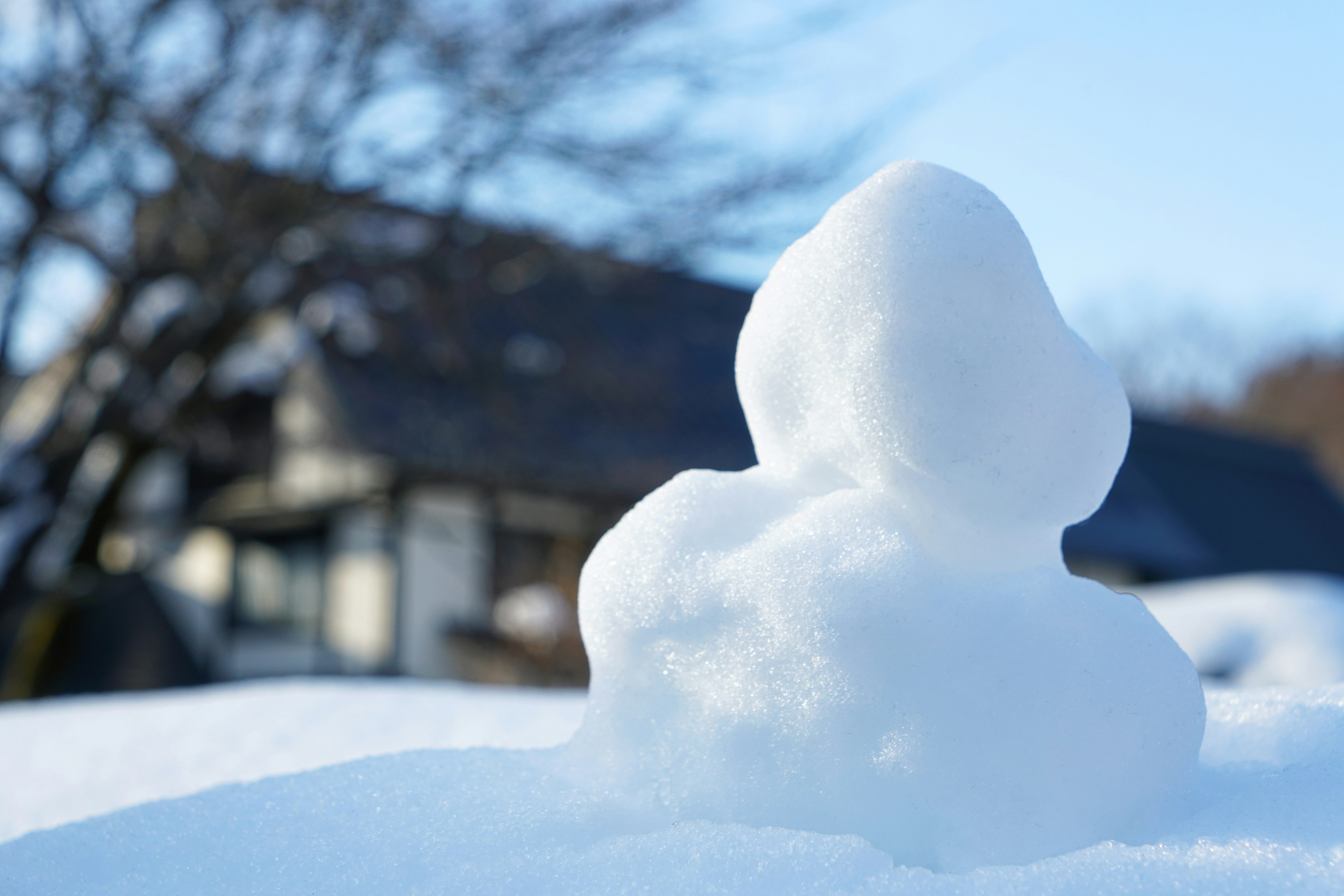 Small snowman made of snow with a house in the background