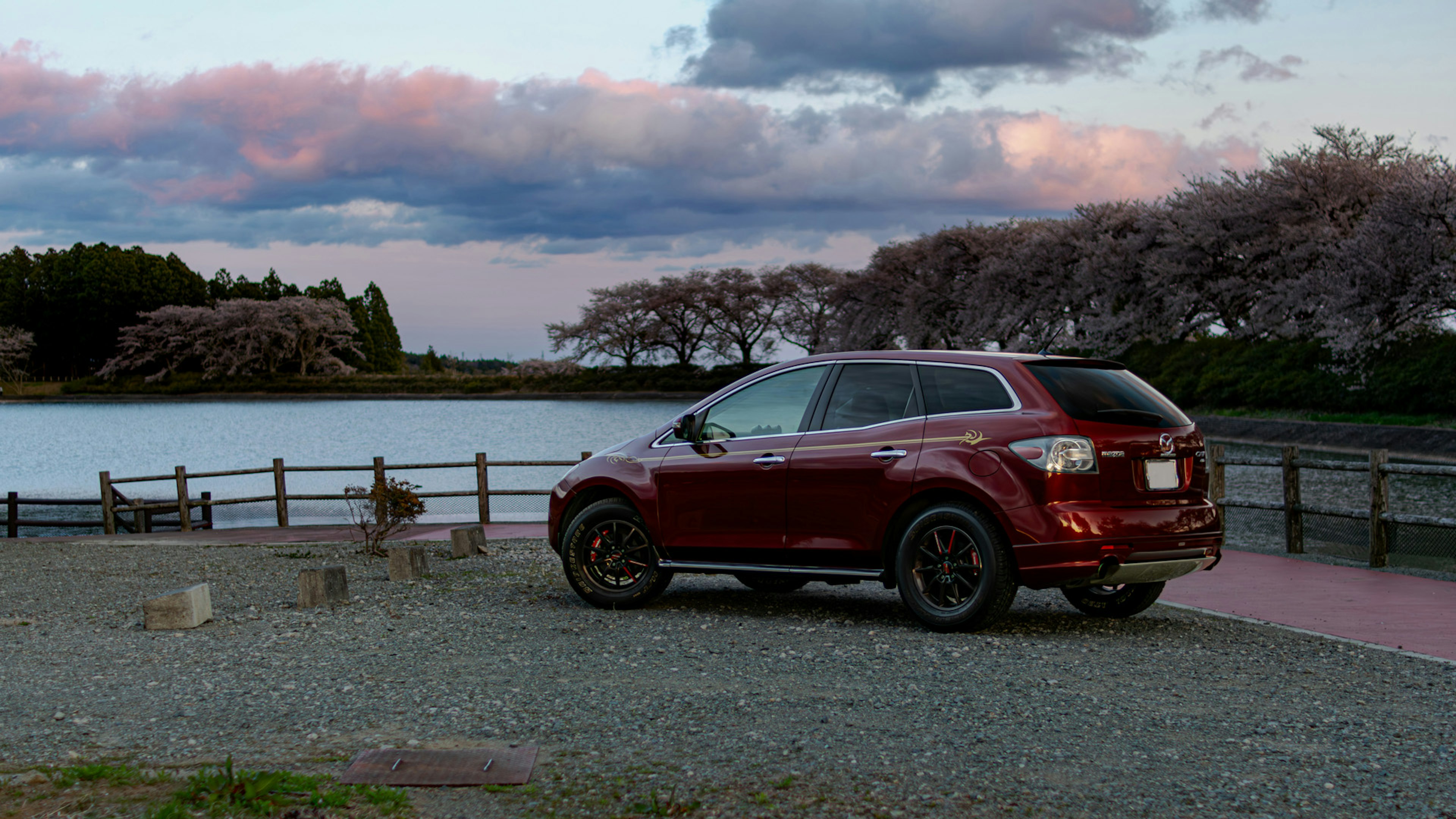 Red SUV parked near a beautiful lake with cherry blossom trees