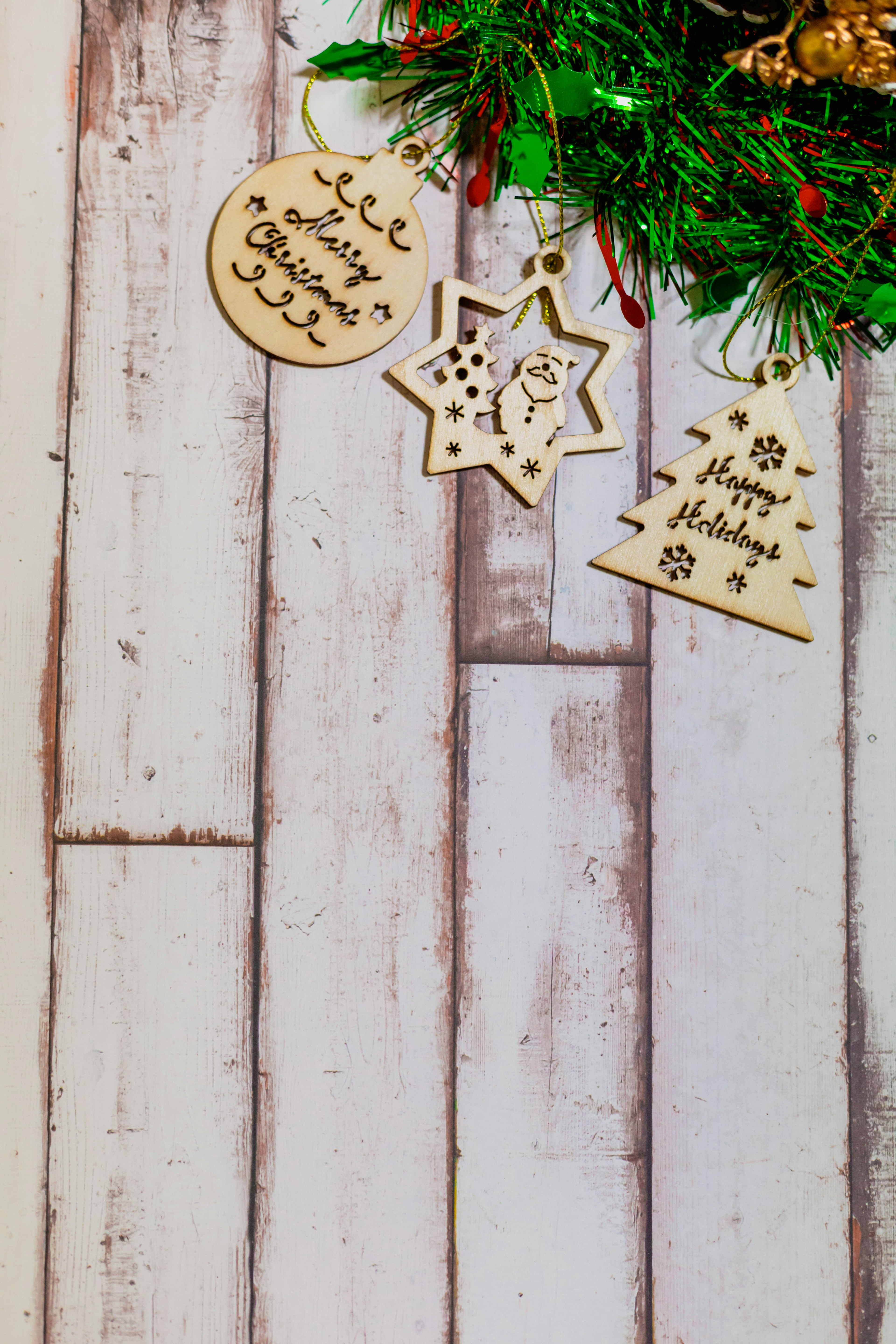 Adornos navideños de madera colgando con una corona verde sobre un fondo de madera