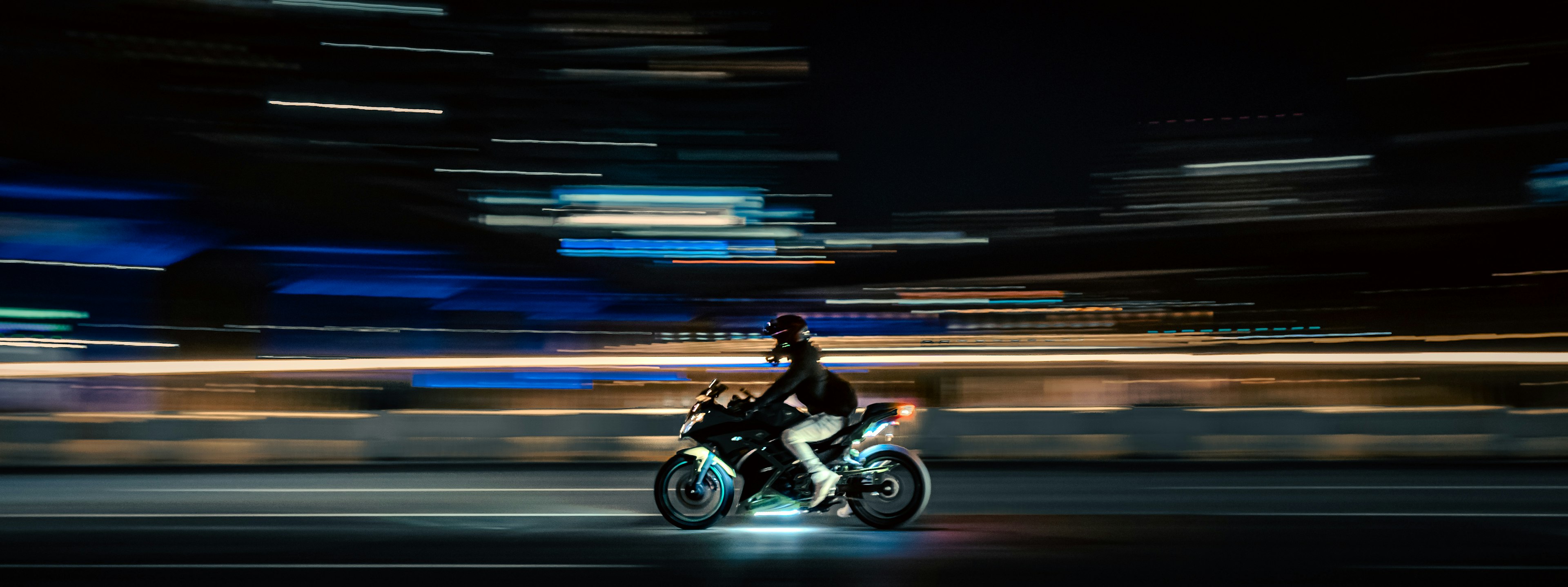 A rider on a motorcycle captured in motion against a blurred city backdrop at night