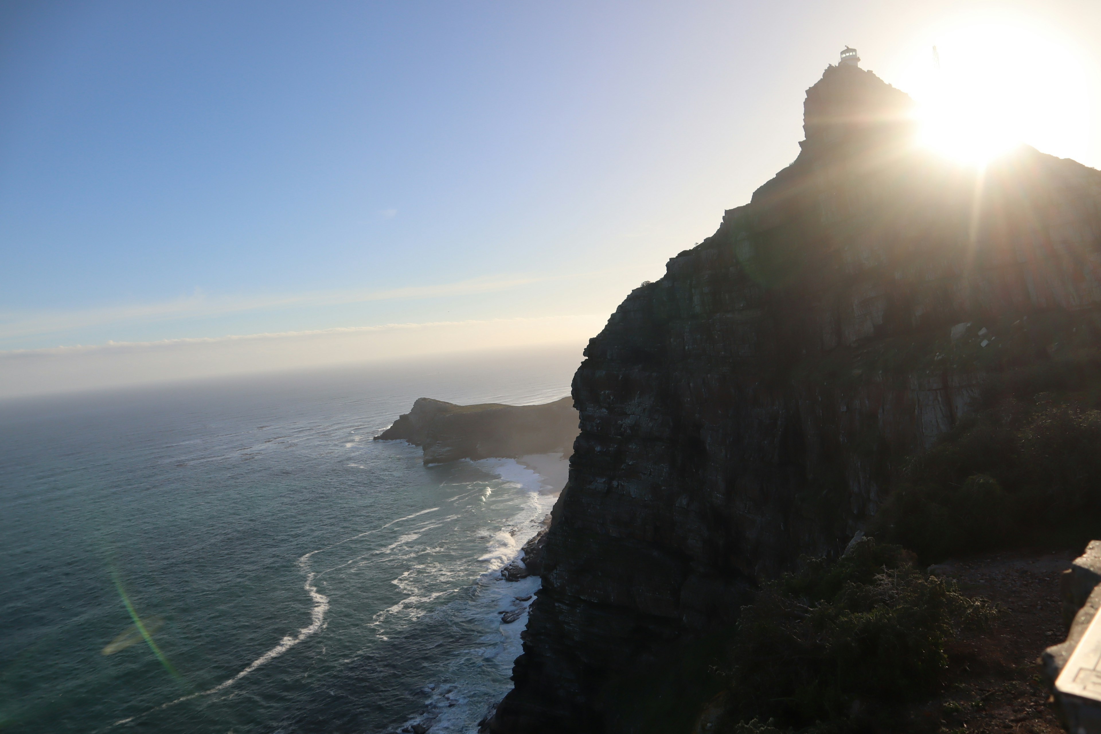 Scenic view of ocean and cliff with a lighthouse at sunset