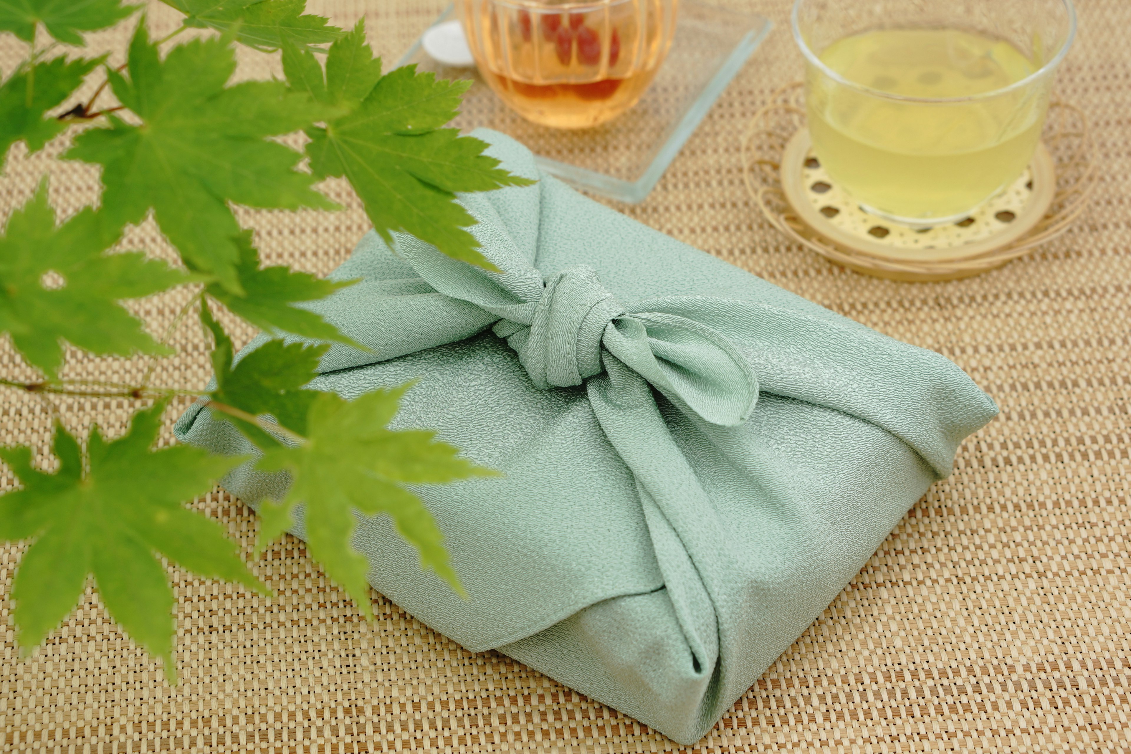 Gift wrapped in light blue fabric next to green leaves and tea