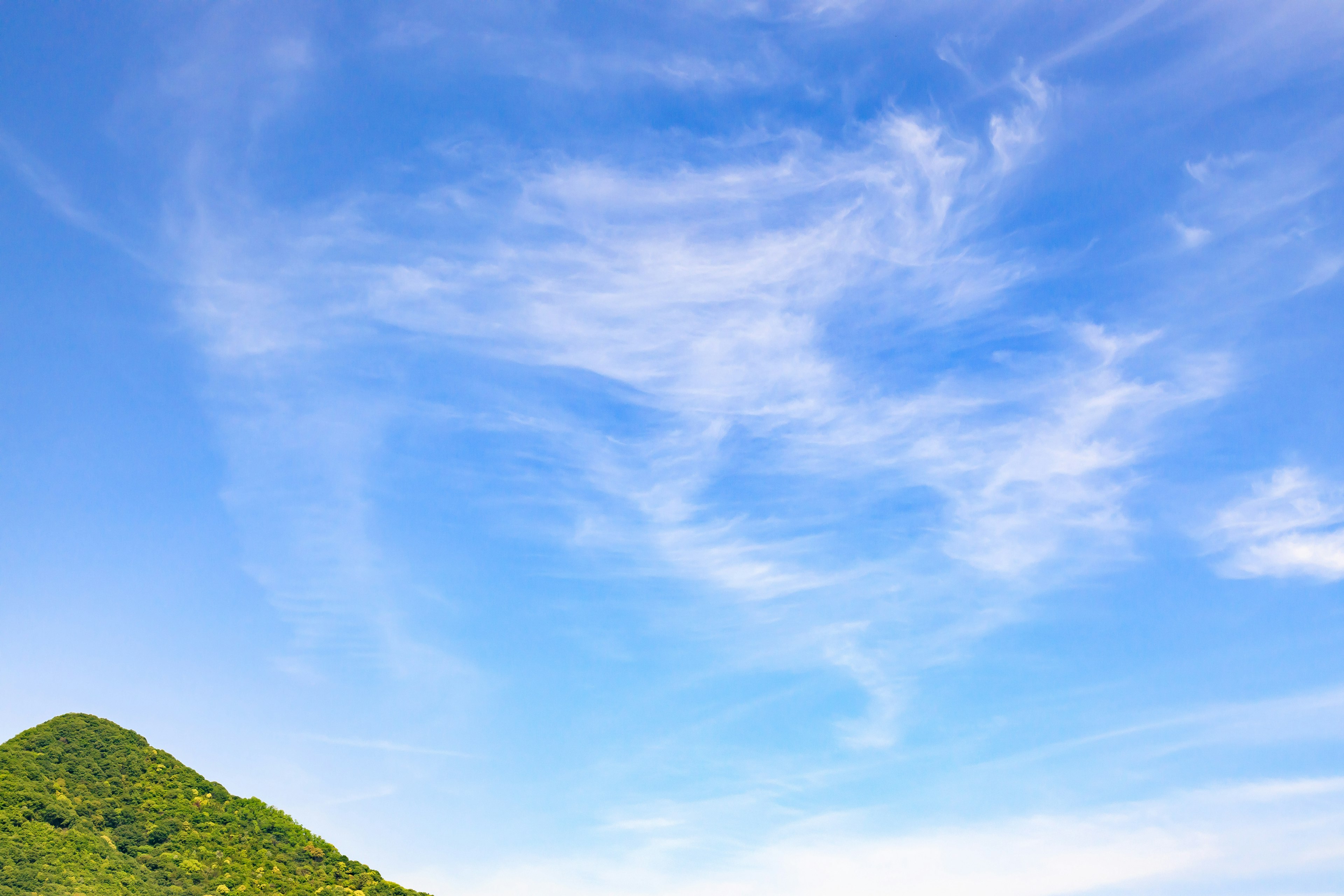 藍天和雲朵的美麗風景，下方有一座綠色的山丘