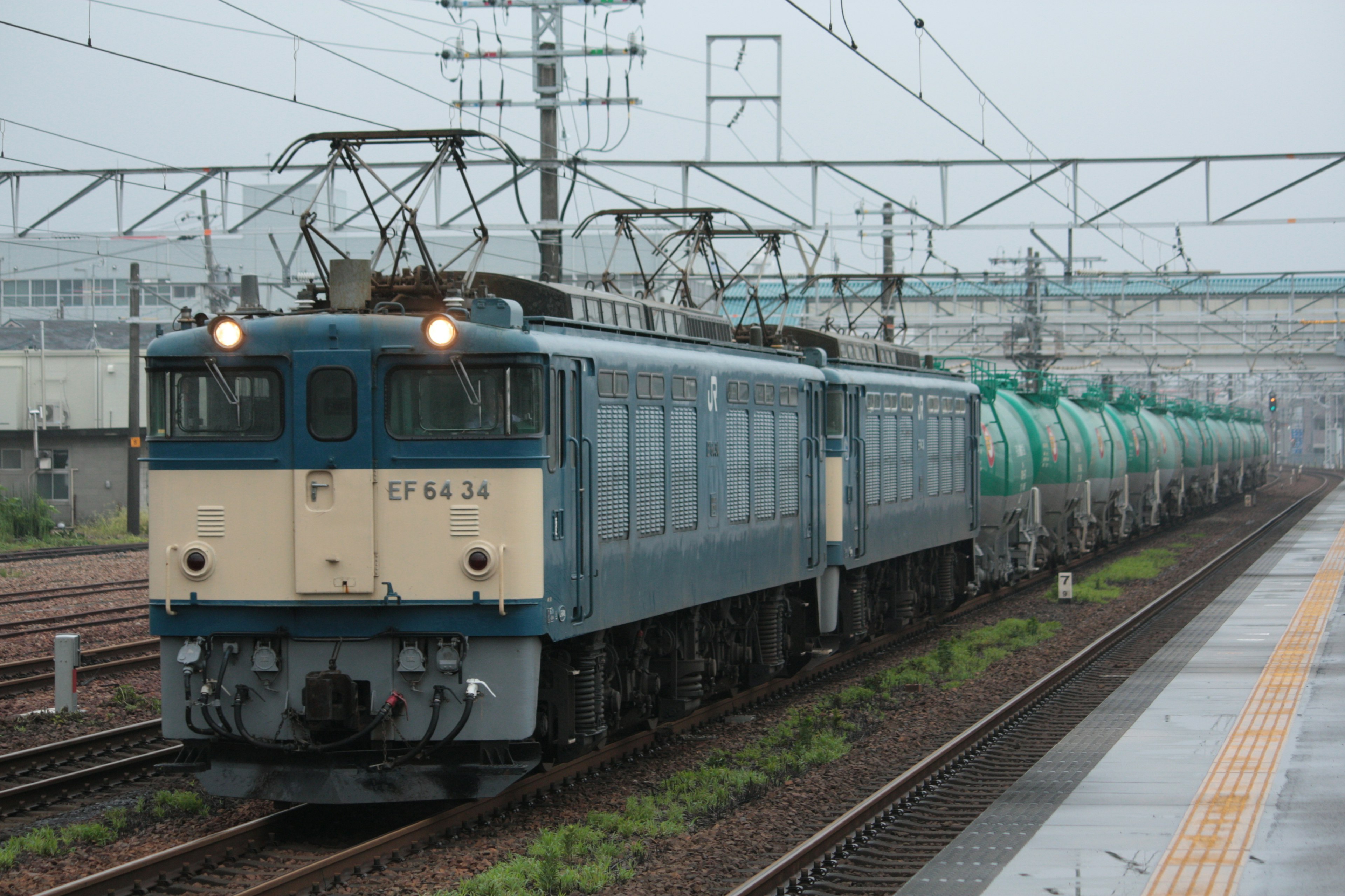 Blue electric locomotive pulling green freight cars on railway tracks