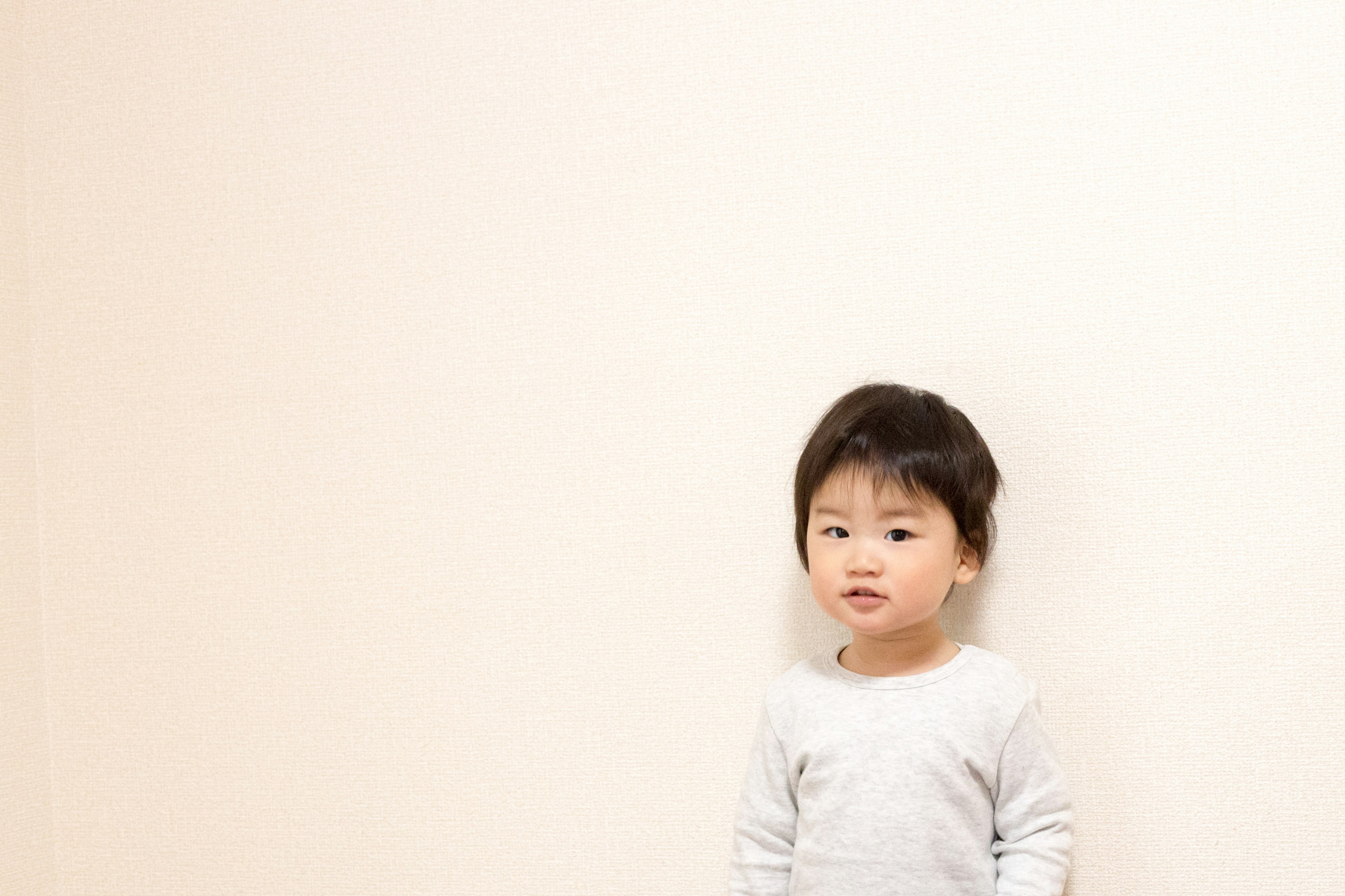 Young boy standing against a wall Glossy hairstyle White long-sleeve shirt