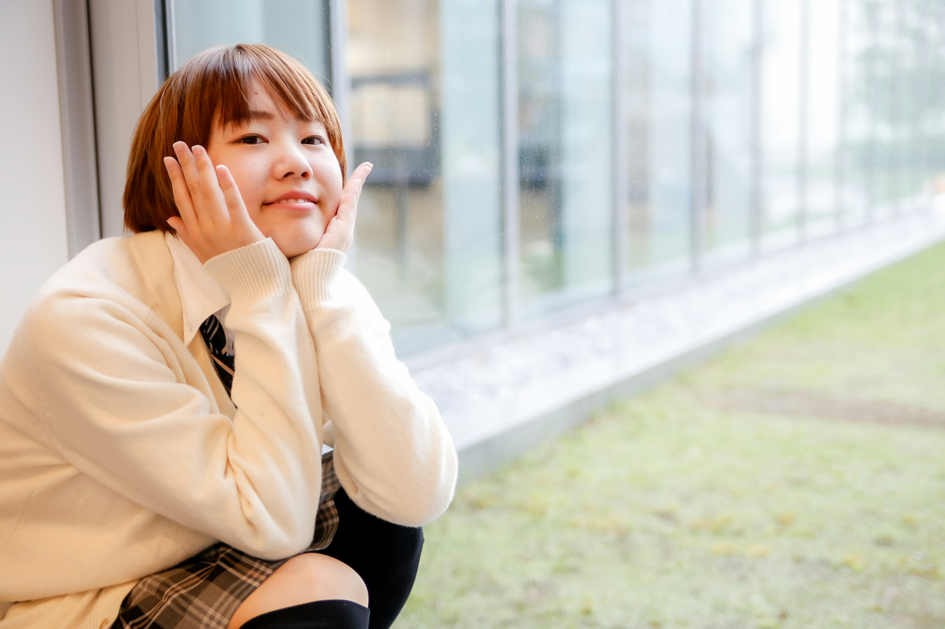 Portrait d'une jeune femme assise près de la fenêtre avec un sourire Elle porte un pull blanc dans un environnement lumineux avec de la lumière naturelle