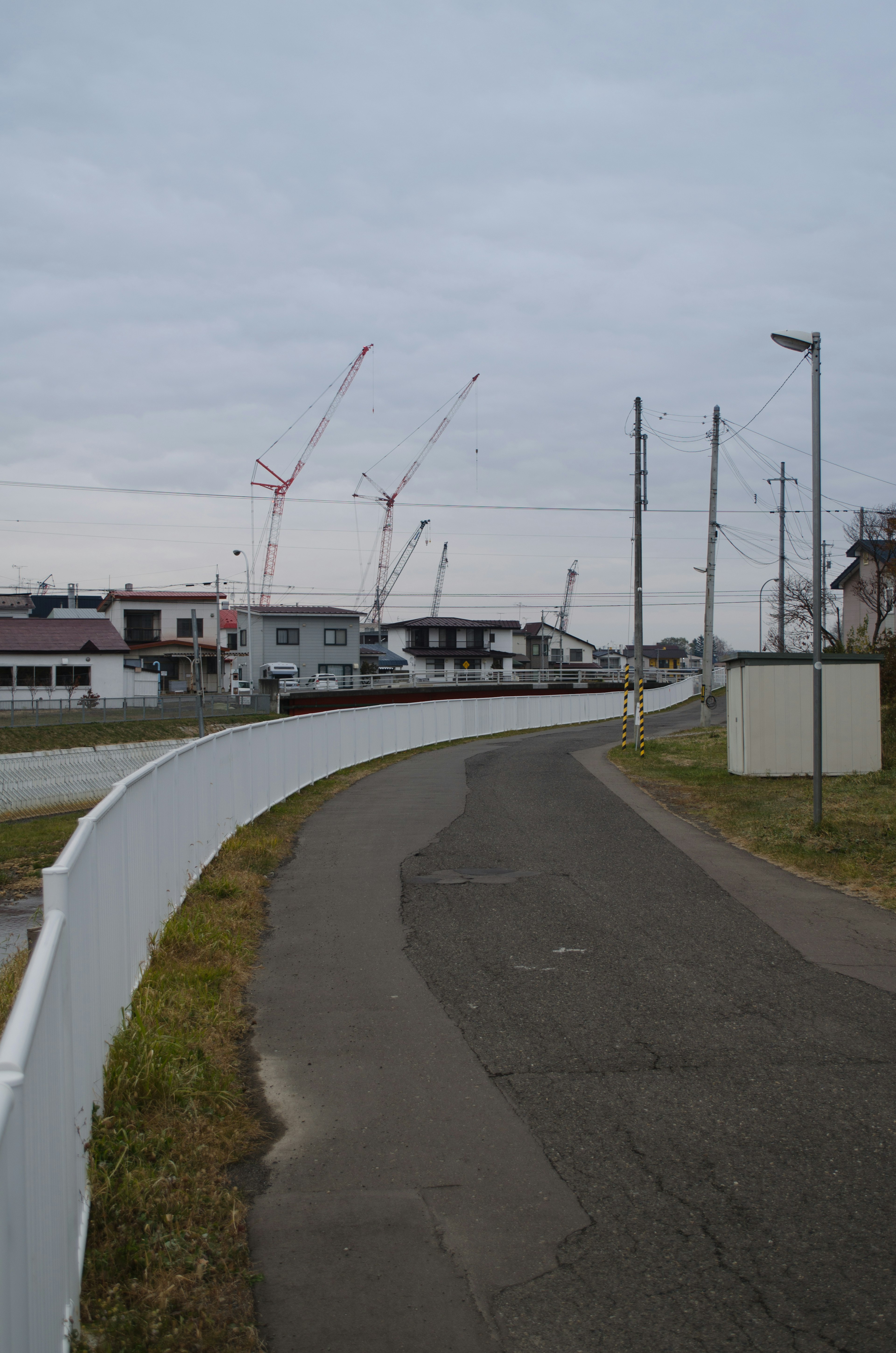 Curved walkway with a construction site featuring cranes under a cloudy sky