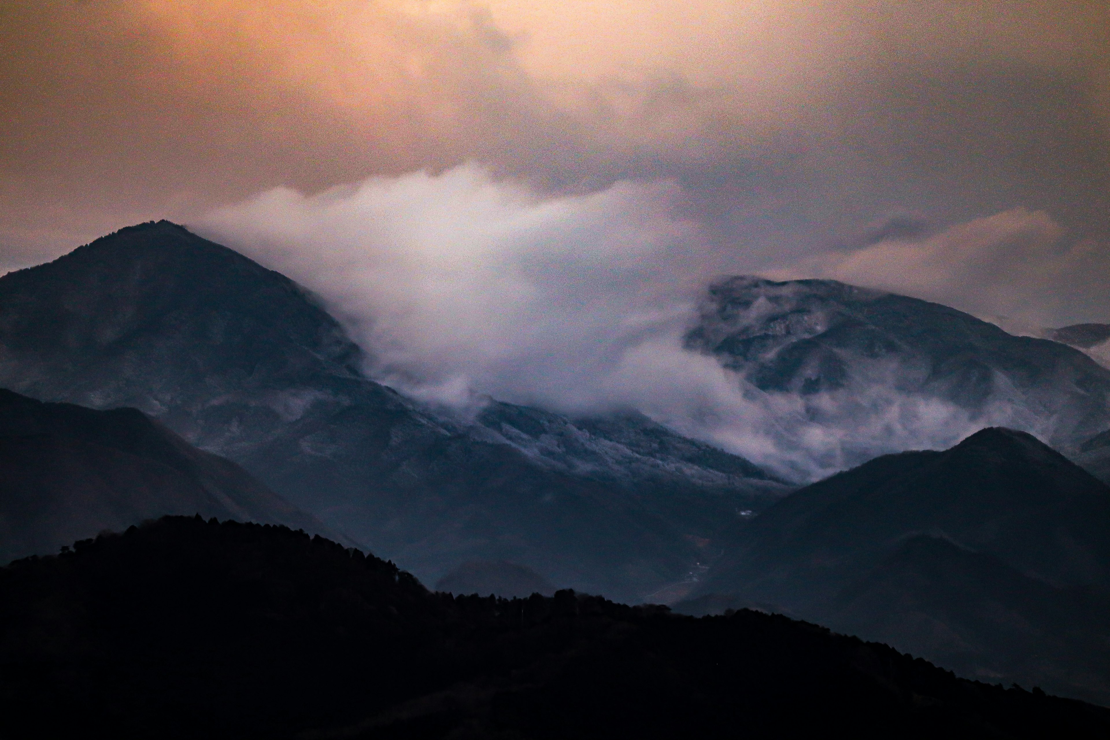 Montagnes enveloppées de brume pendant le coucher de soleil avec des nuages doux