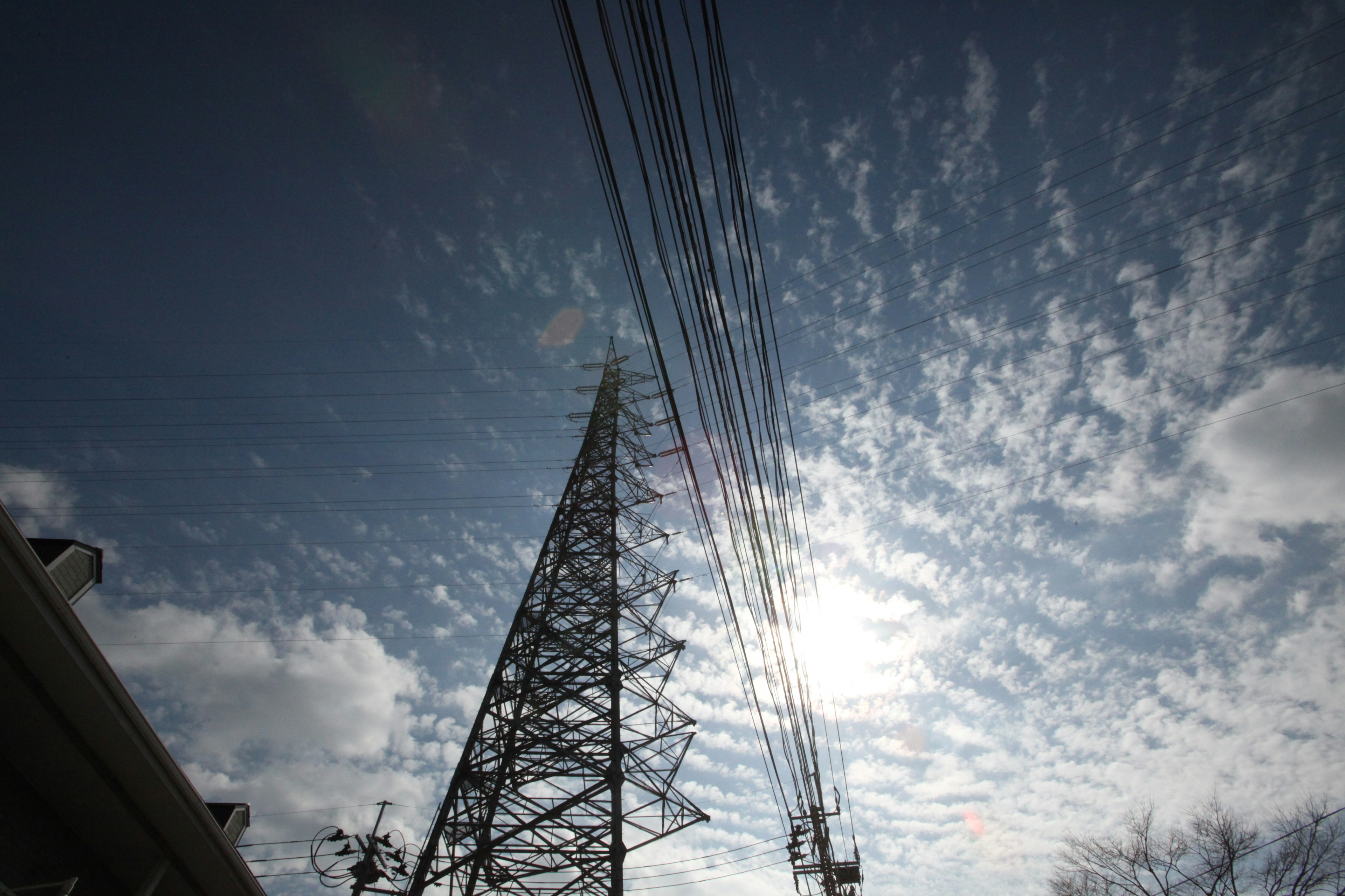 High-voltage power tower under a blue sky with clouds