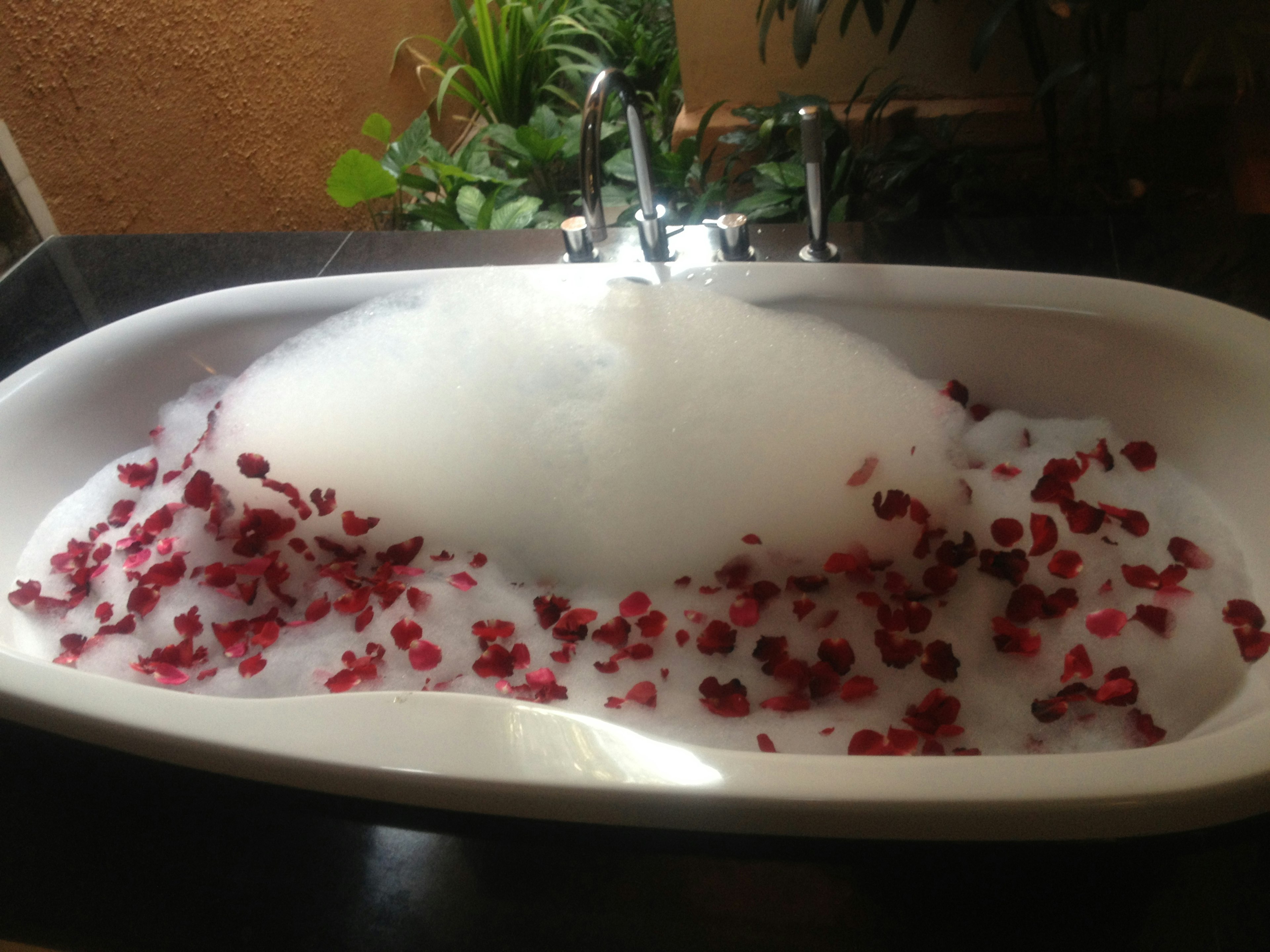 A bathtub filled with bubbles and floating red flower petals