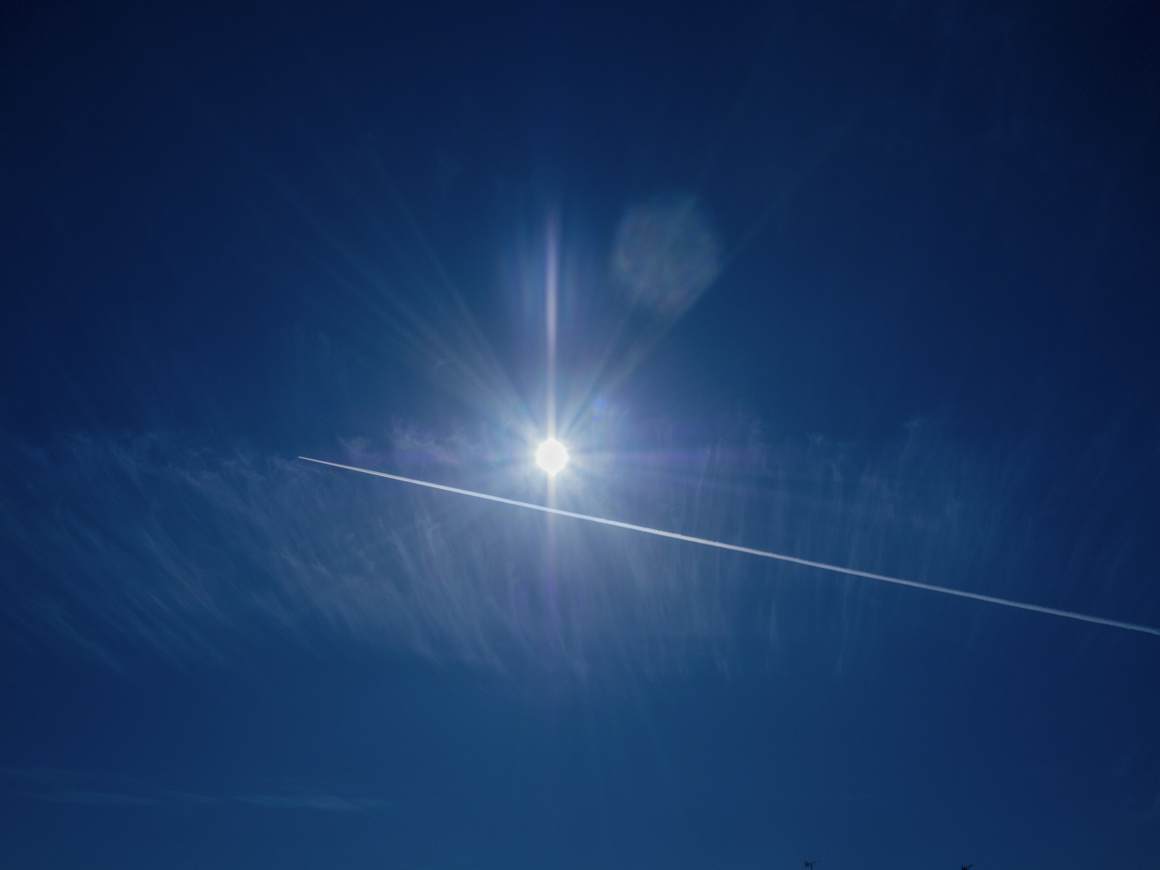 Bright sun shining in a clear blue sky with a contrail