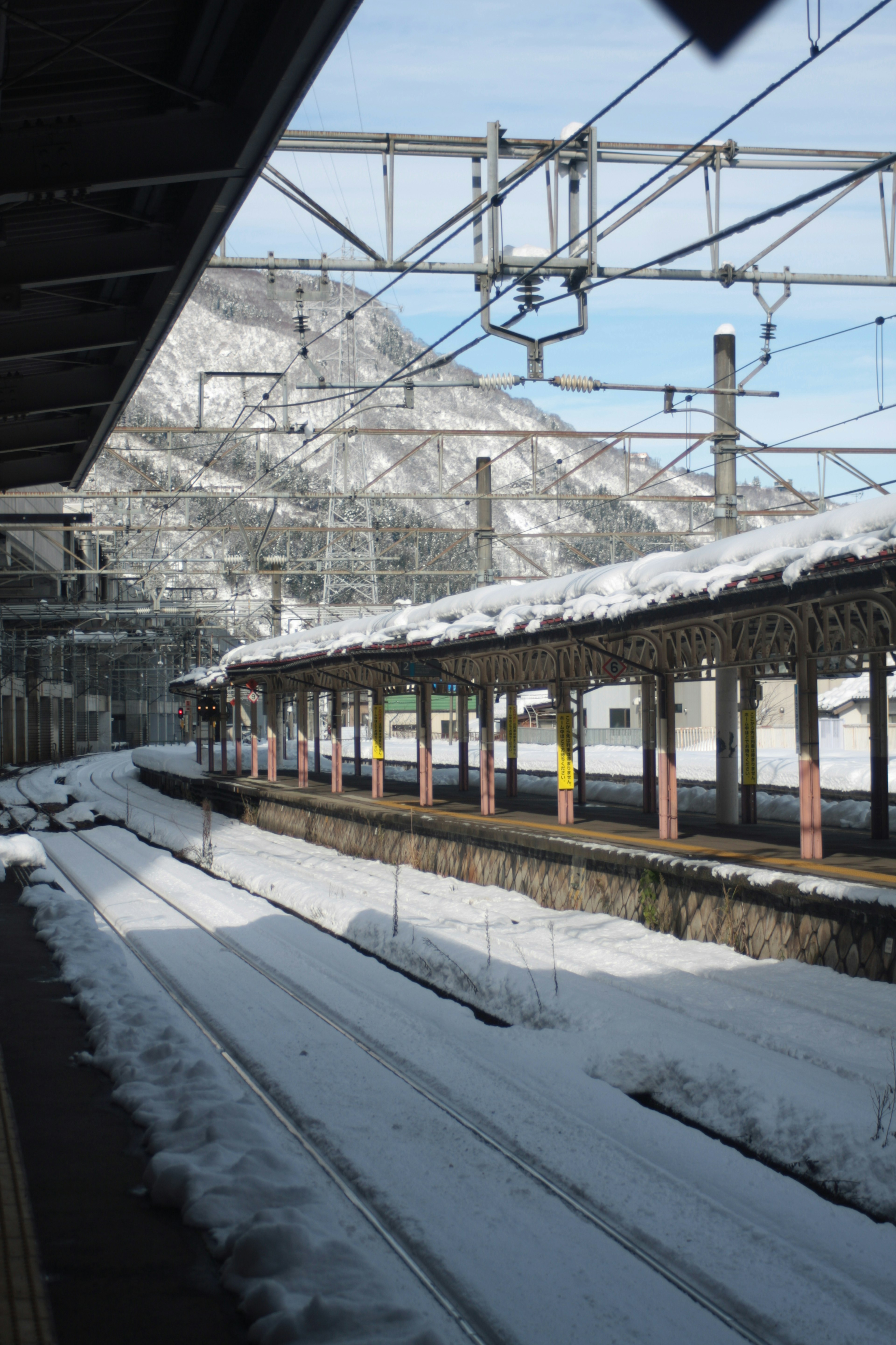 Snow-covered train station platform with tracks and mountainous background