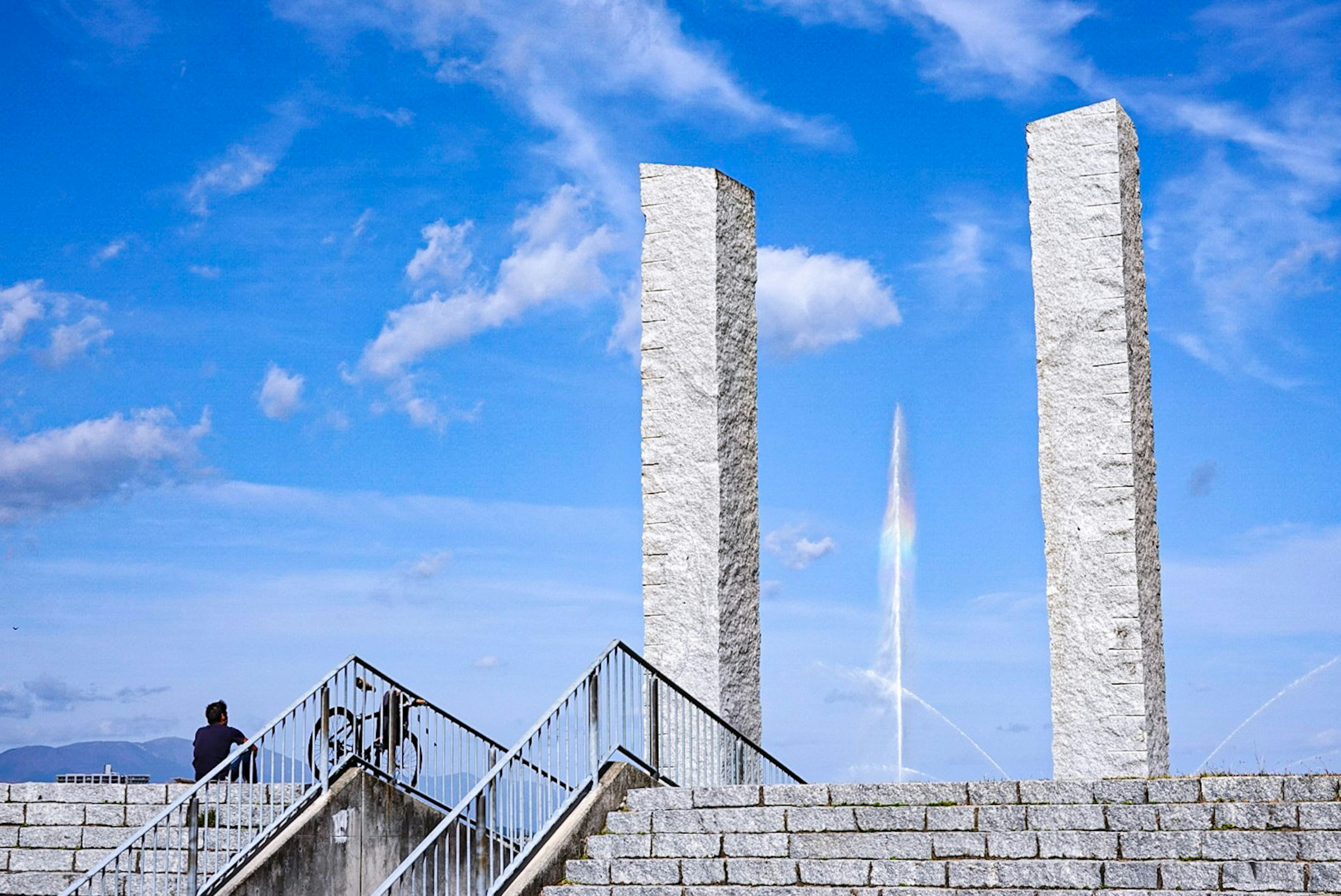 Deux piliers de pierre blancs sous un ciel bleu avec une personne sur des escaliers