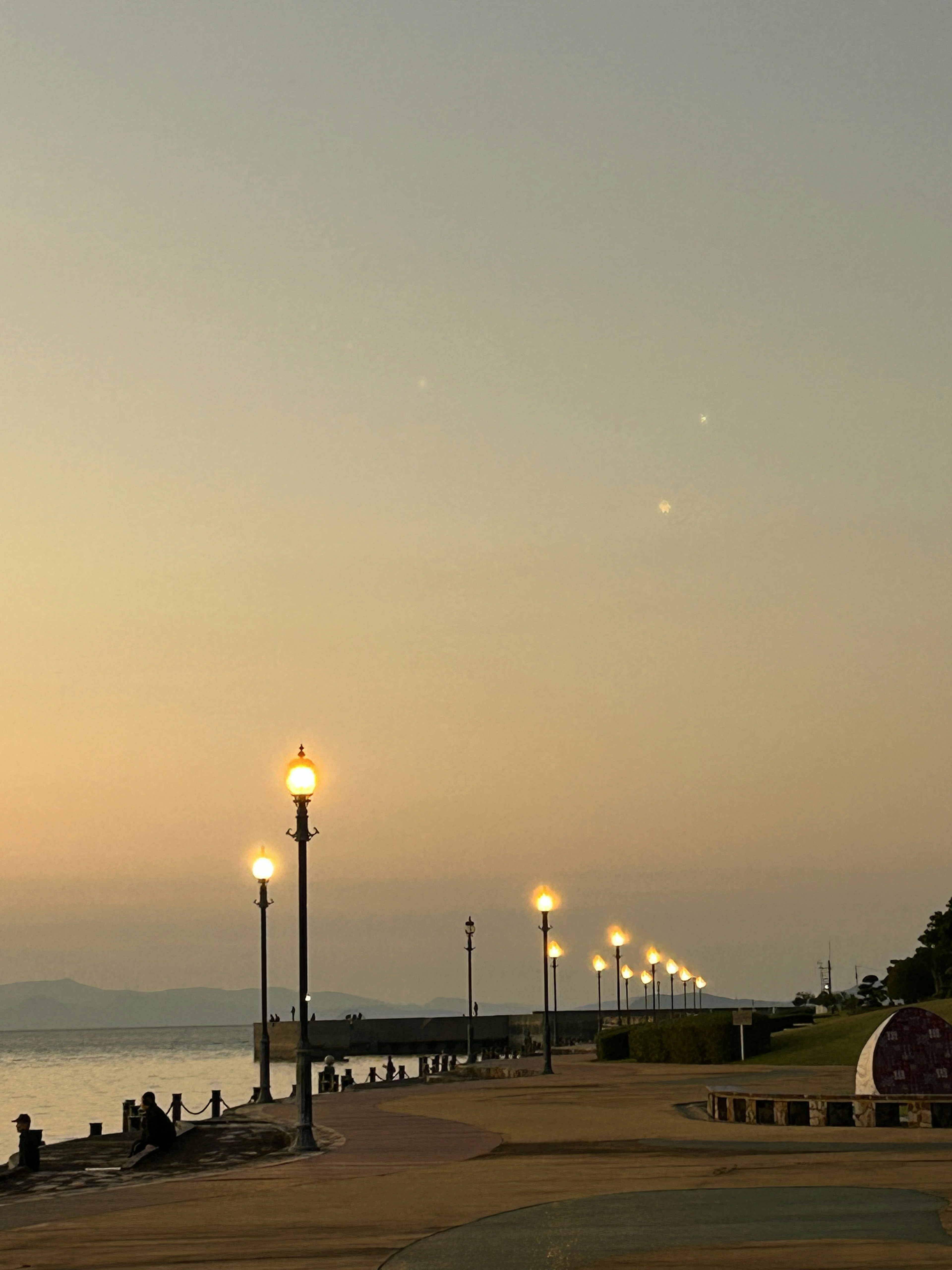 A waterfront promenade illuminated by streetlights at dusk