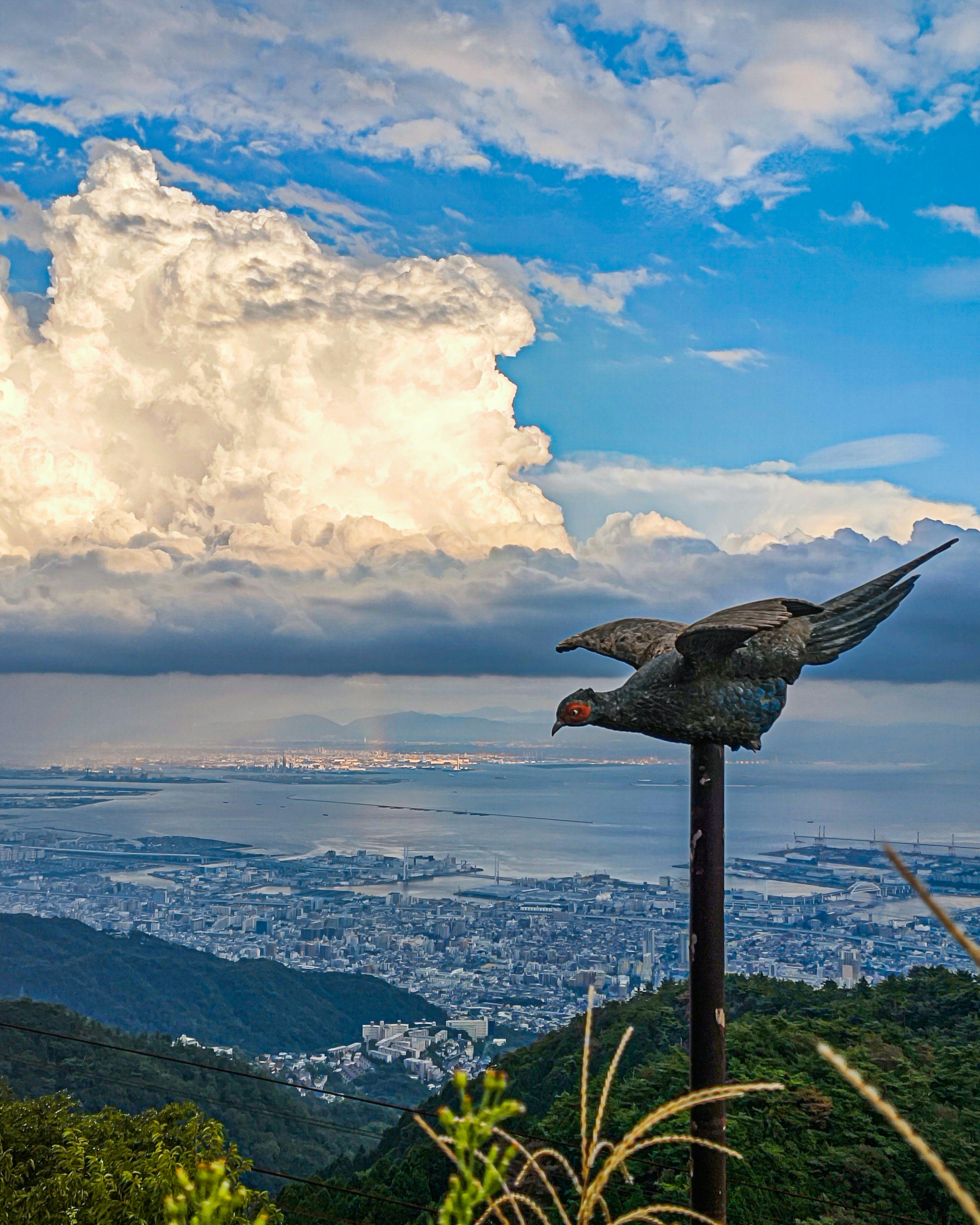 Mountain landscape with a bird sculpture taking flight against a blue sky and clouds