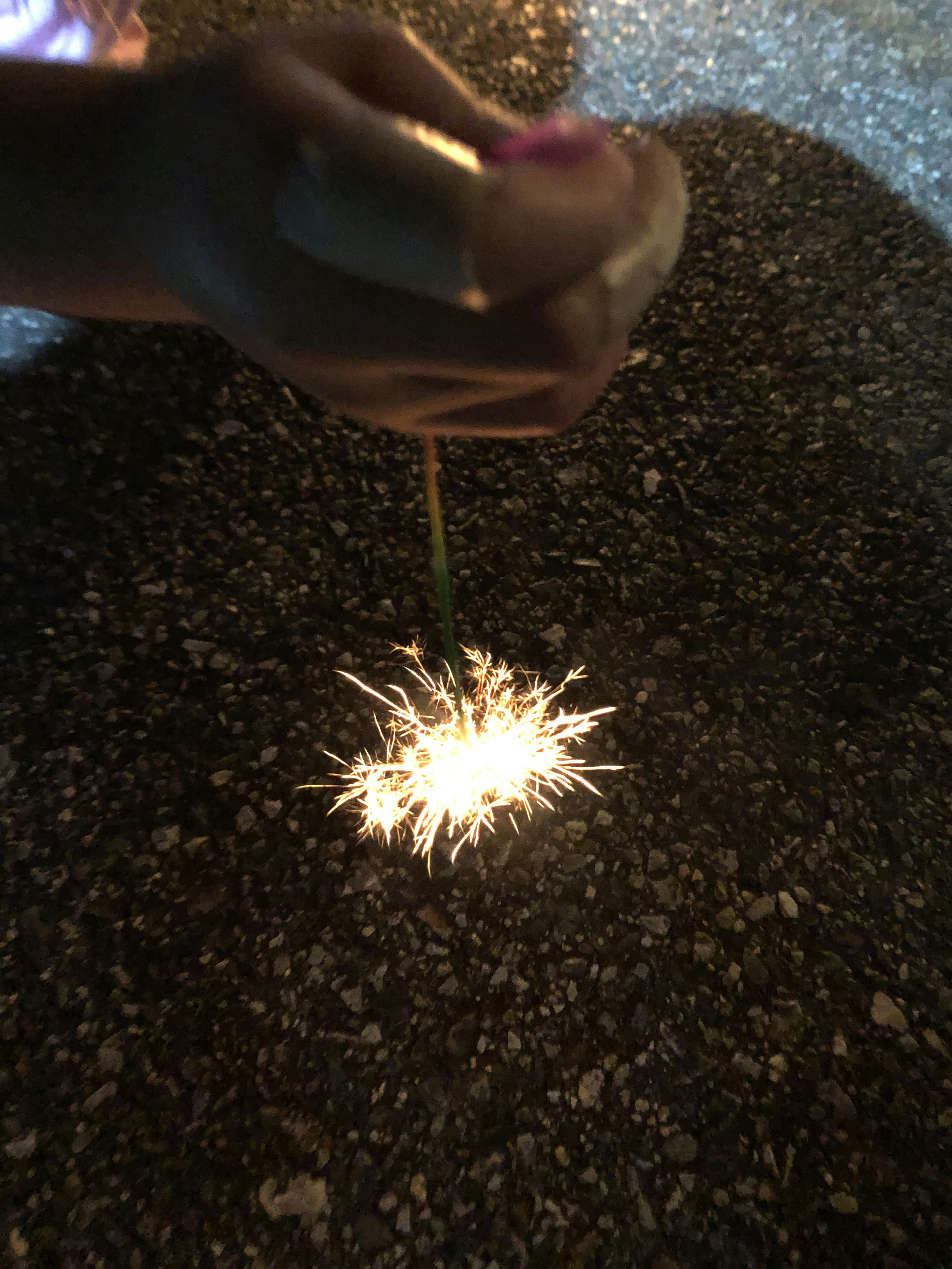 Un fuego artificial sostenido en la mano brillando en el suelo por la noche