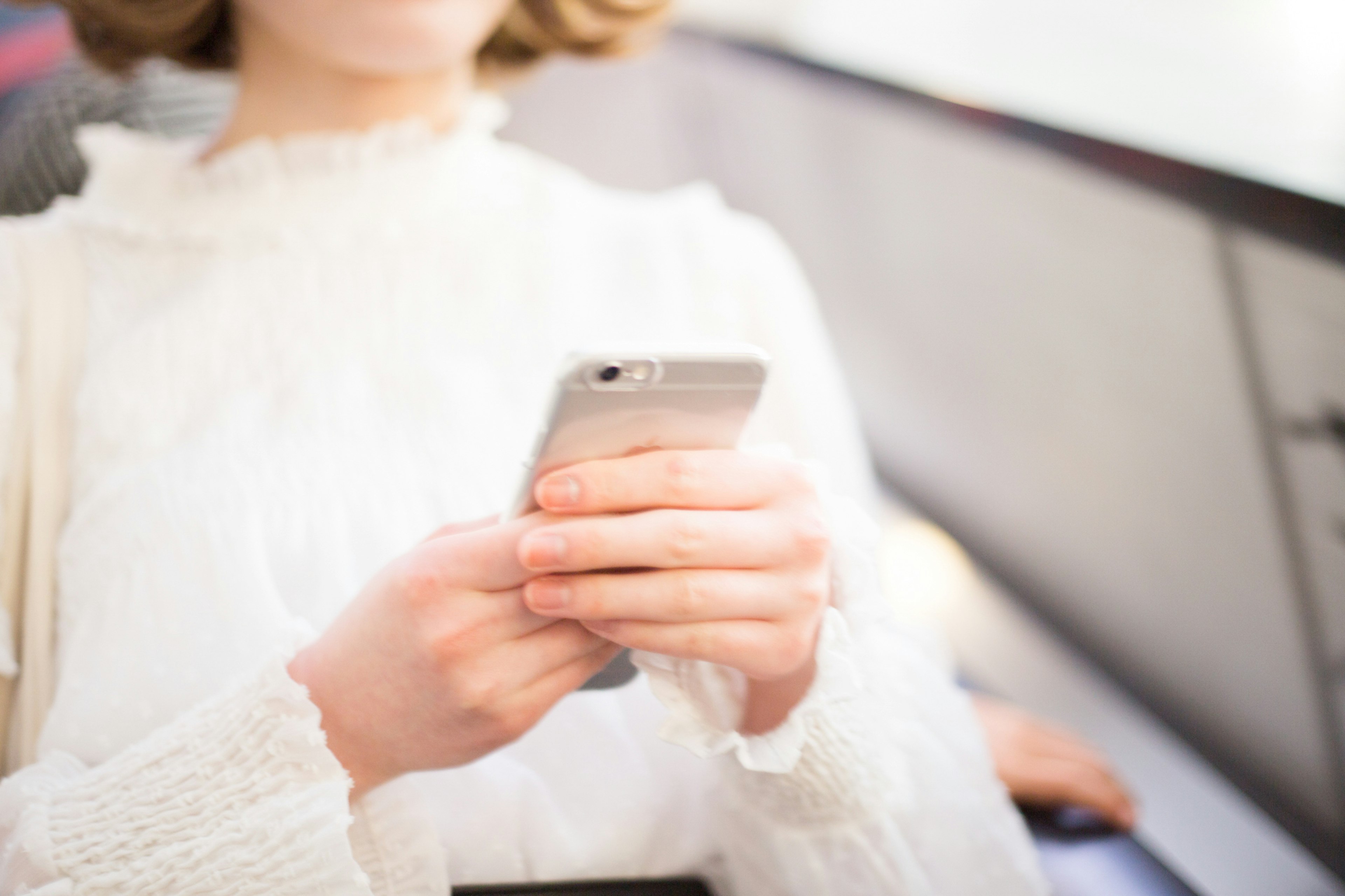 Mujer con suéter blanco usando un teléfono inteligente