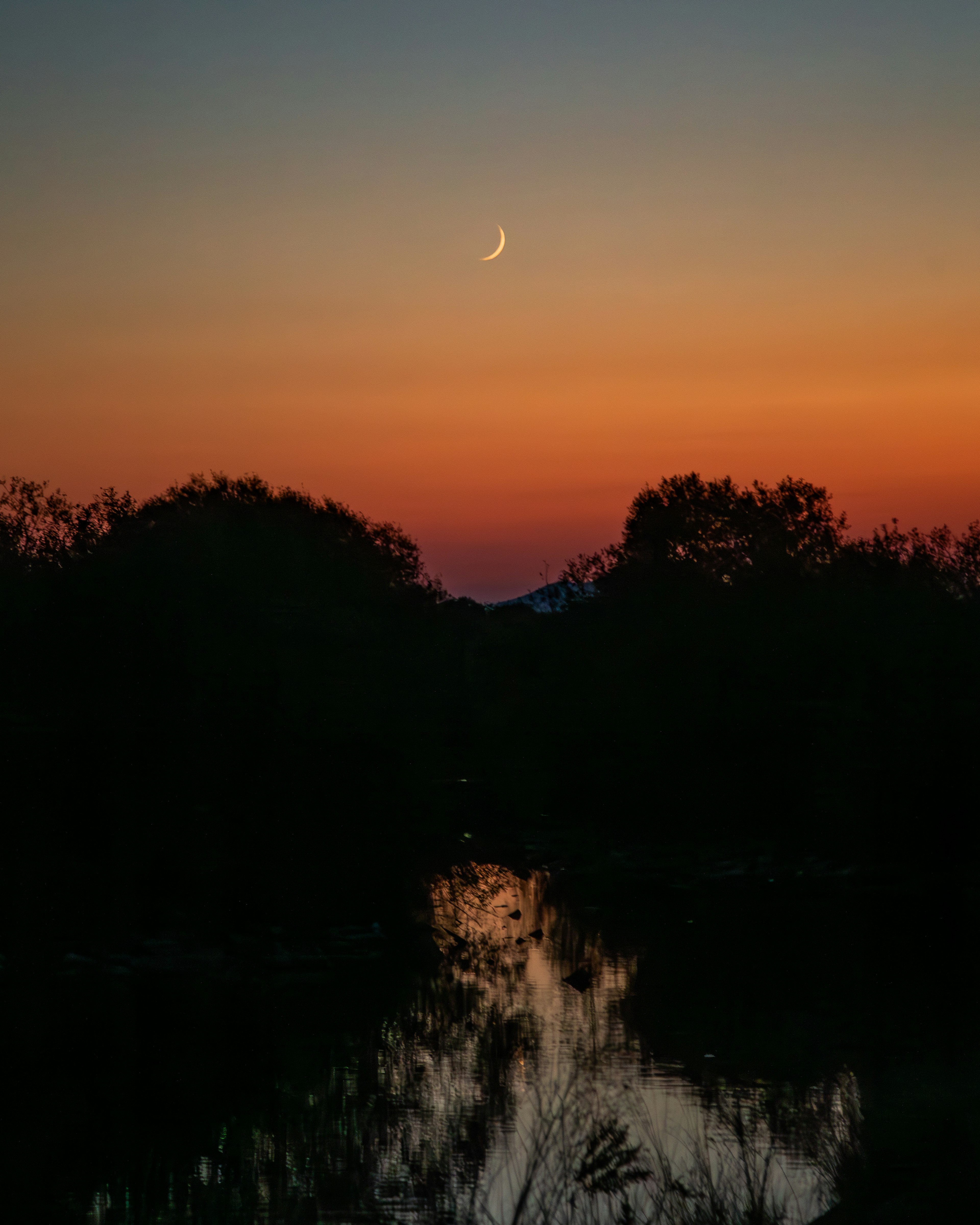 A crescent moon in twilight over a tranquil lake