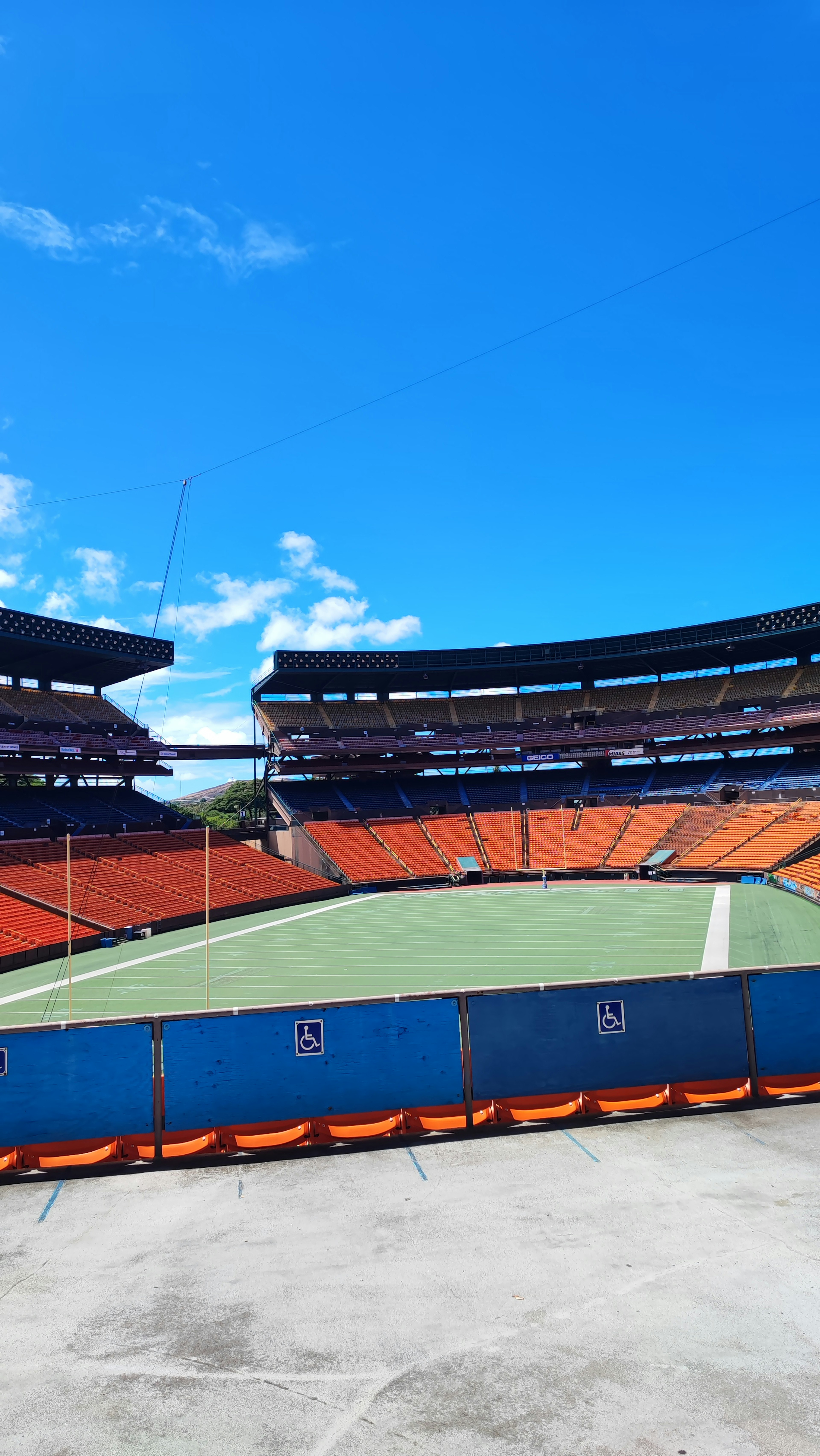 Interior of a stadium with orange seating under a clear blue sky