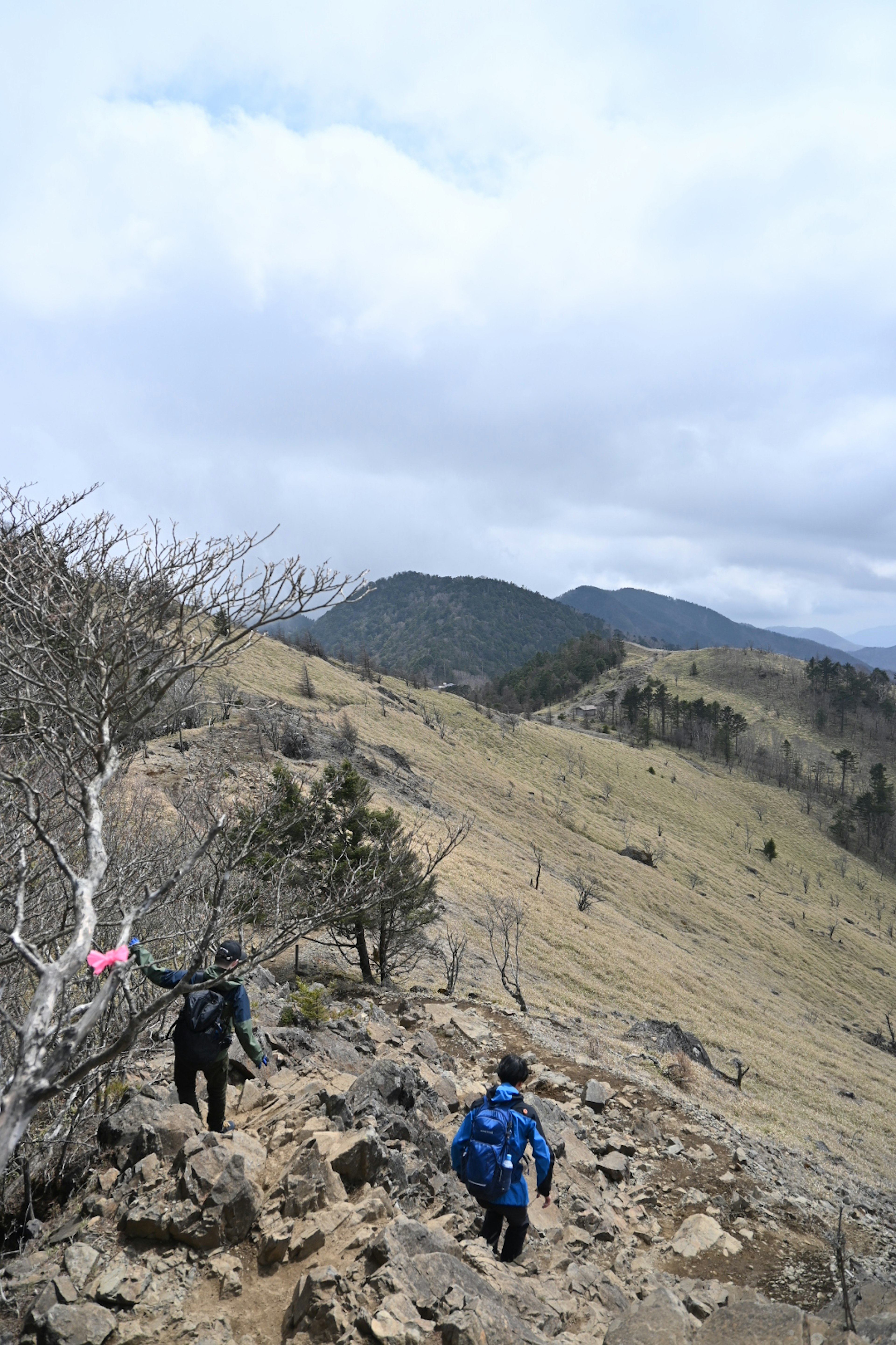 Dos excursionistas ascendiendo por un sendero rocoso bajo un cielo nublado