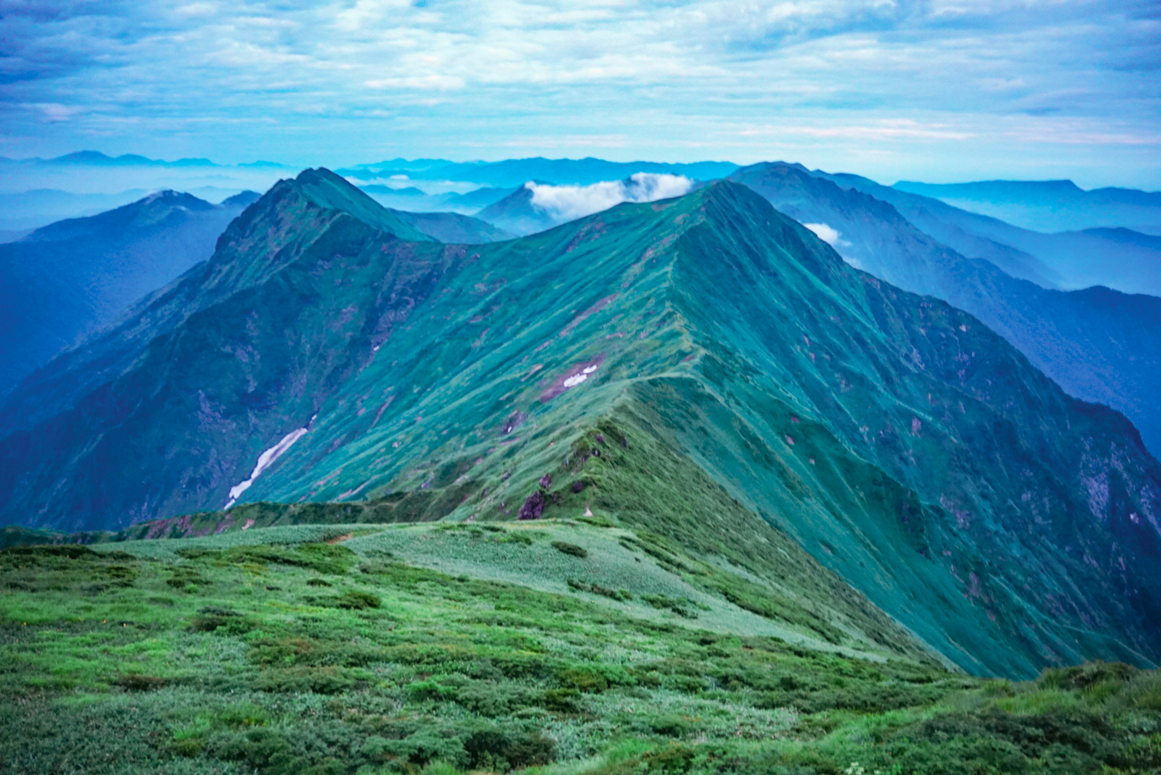 Vista panoramica di vette montuose verdeggianti sotto un cielo blu con nuvole