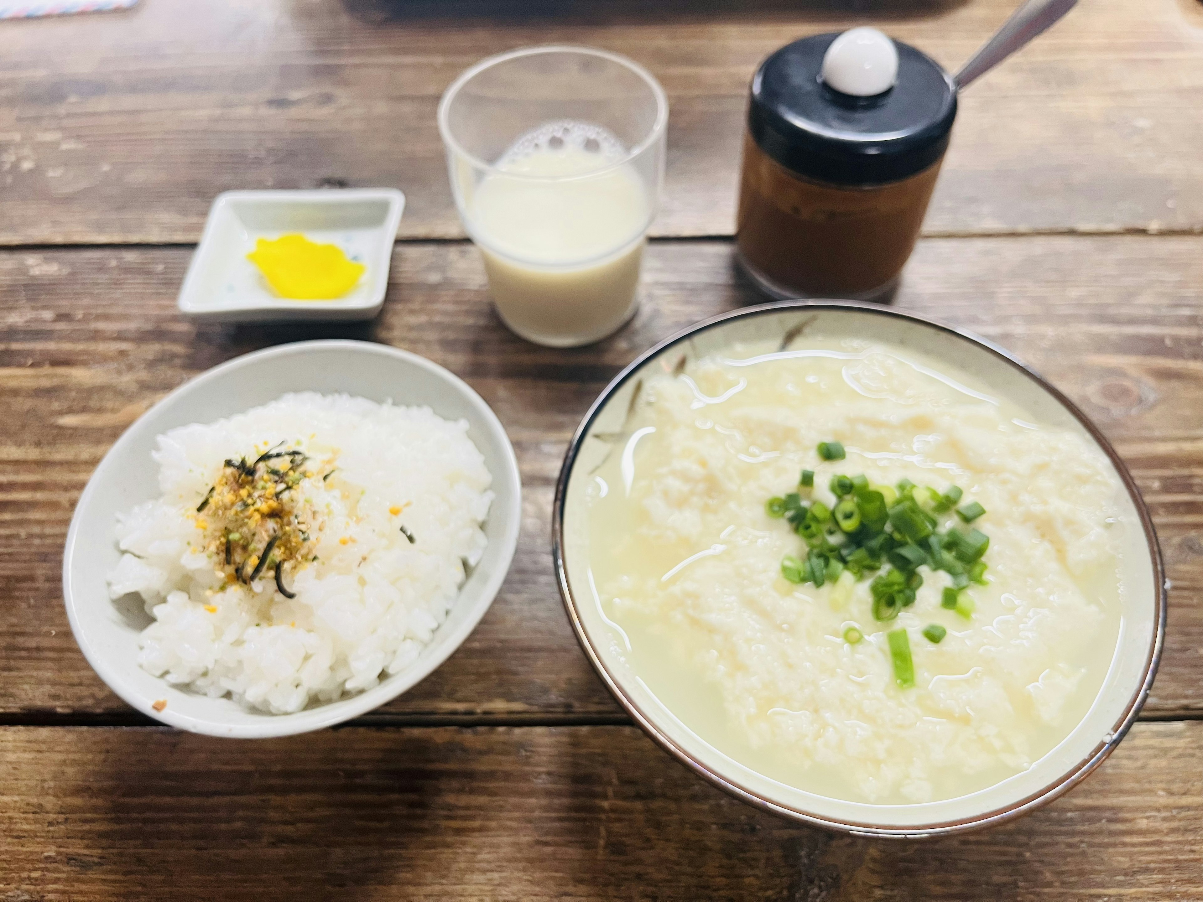 Un tazón de sopa caliente con cebollas verdes y un acompañamiento de arroz sobre una mesa de madera