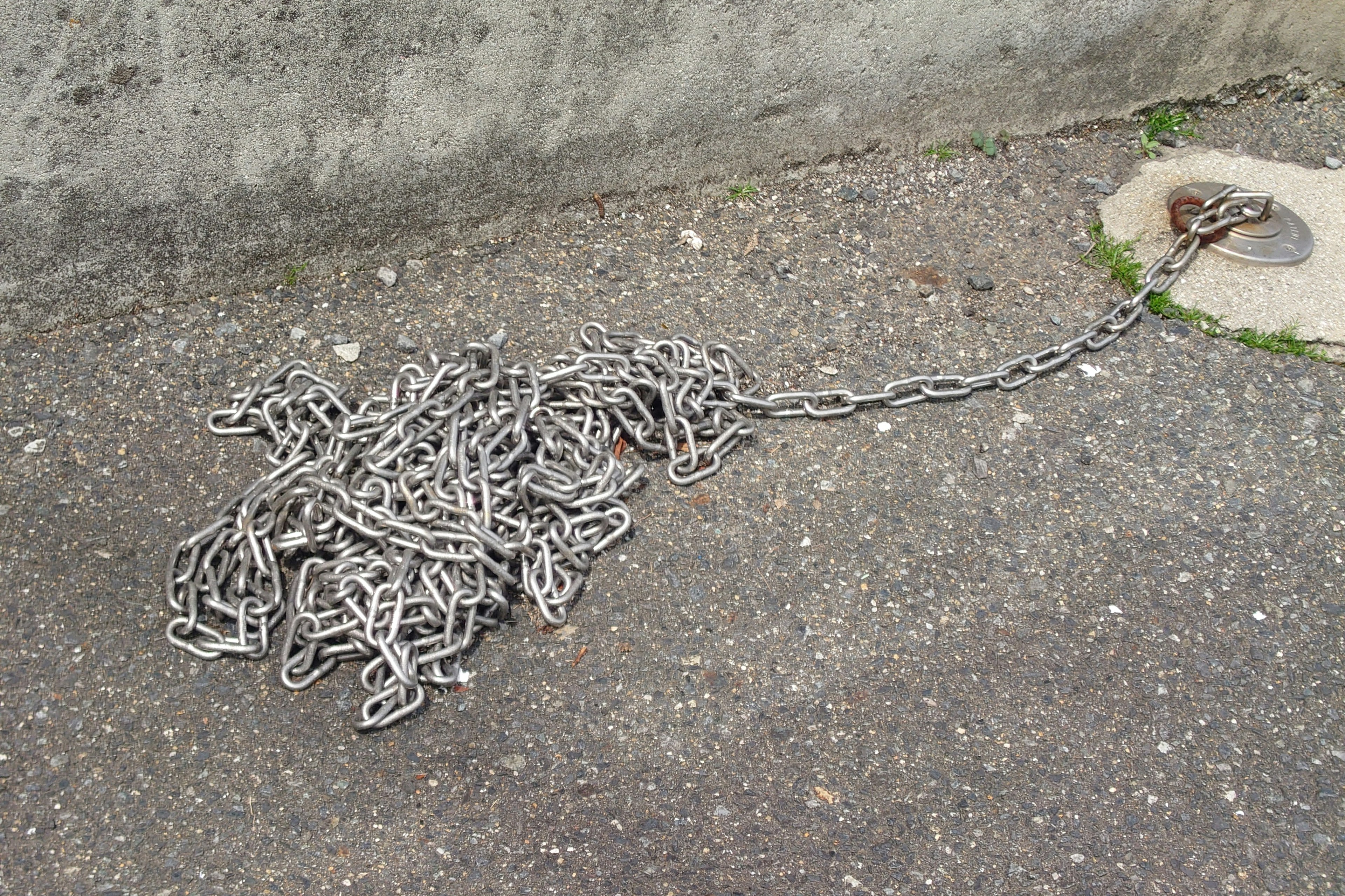 A tangled mass of metal chains on the ground next to a concrete post