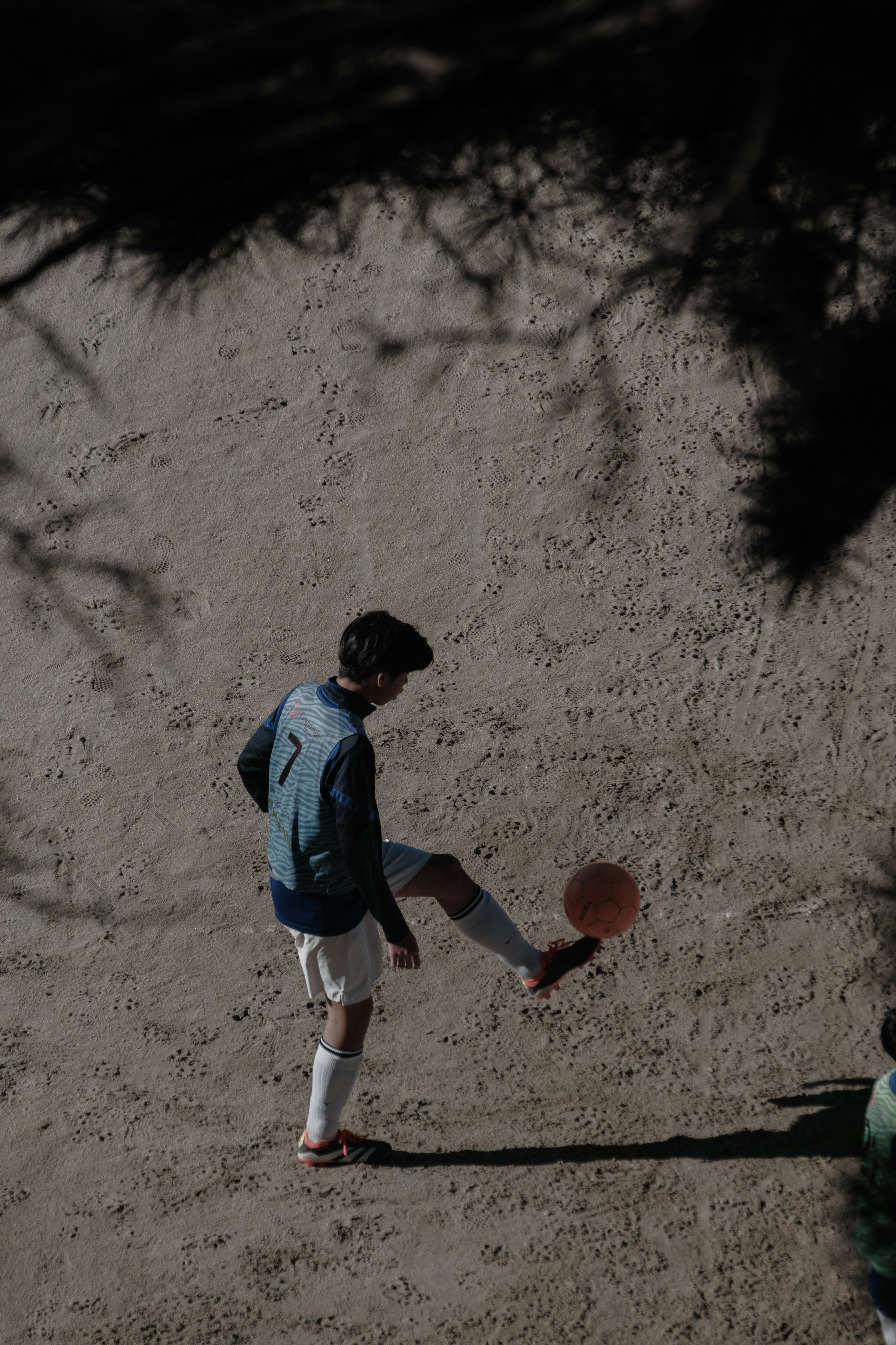 Silhouette eines Jungen, der einen Fußball auf einem sandigen Feld tritt