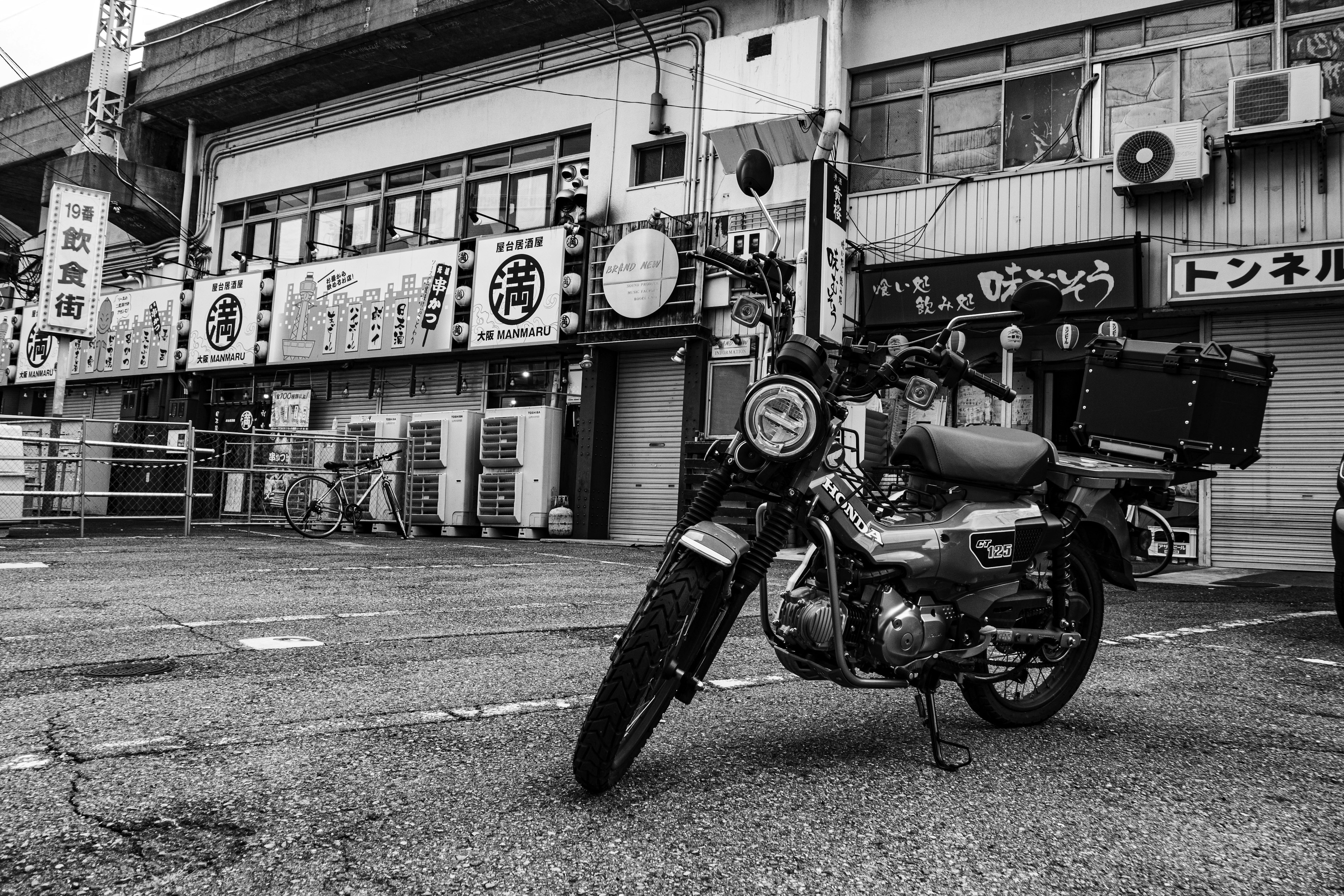 Black and white photo of a motorcycle parked in a Japanese urban setting