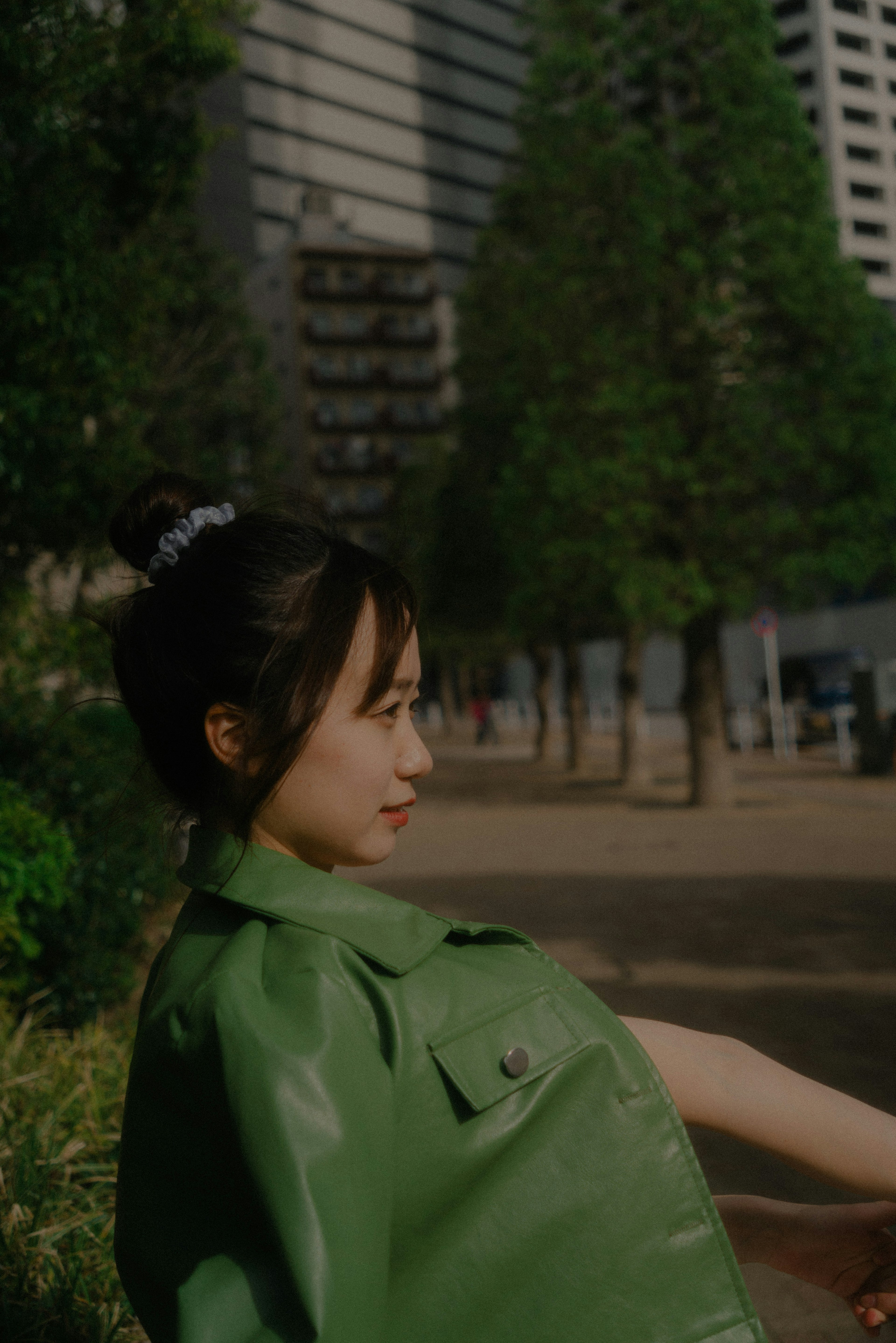 A woman in a green jacket looking sideways in a park