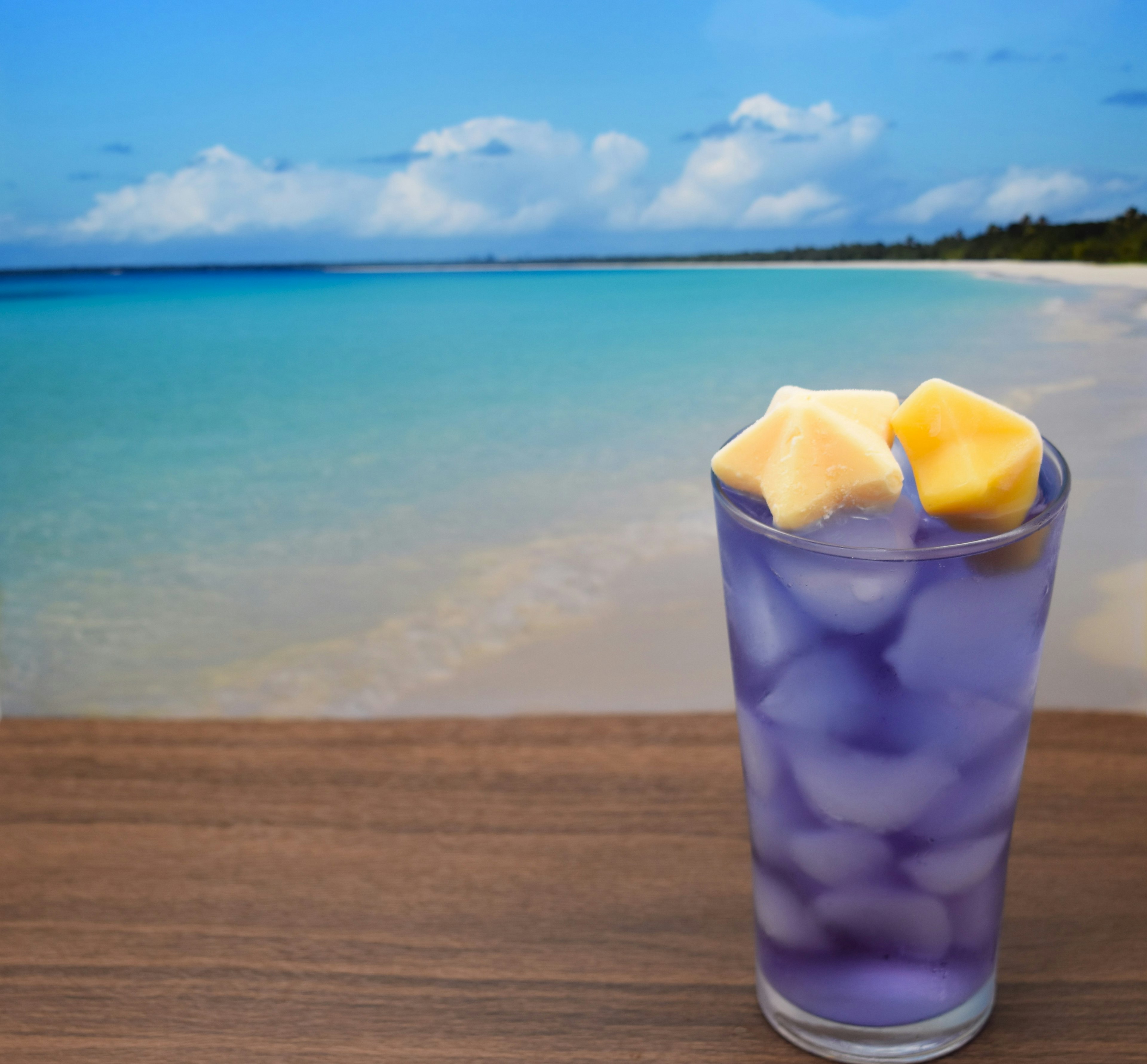 Bebida morada con hielo en un vaso con fondo de playa