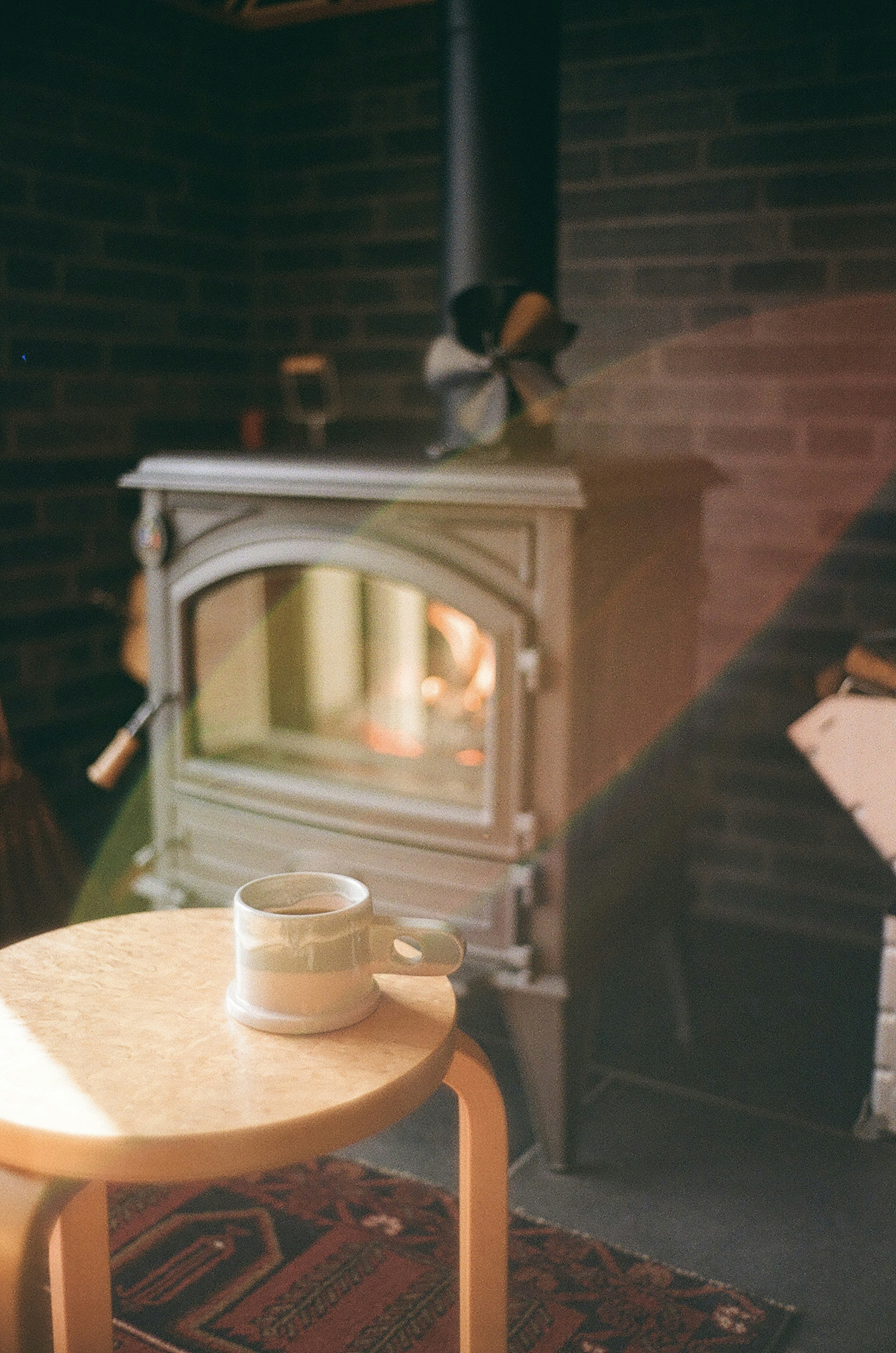 Wooden table with a cup in front of a stove warm light in a cozy space